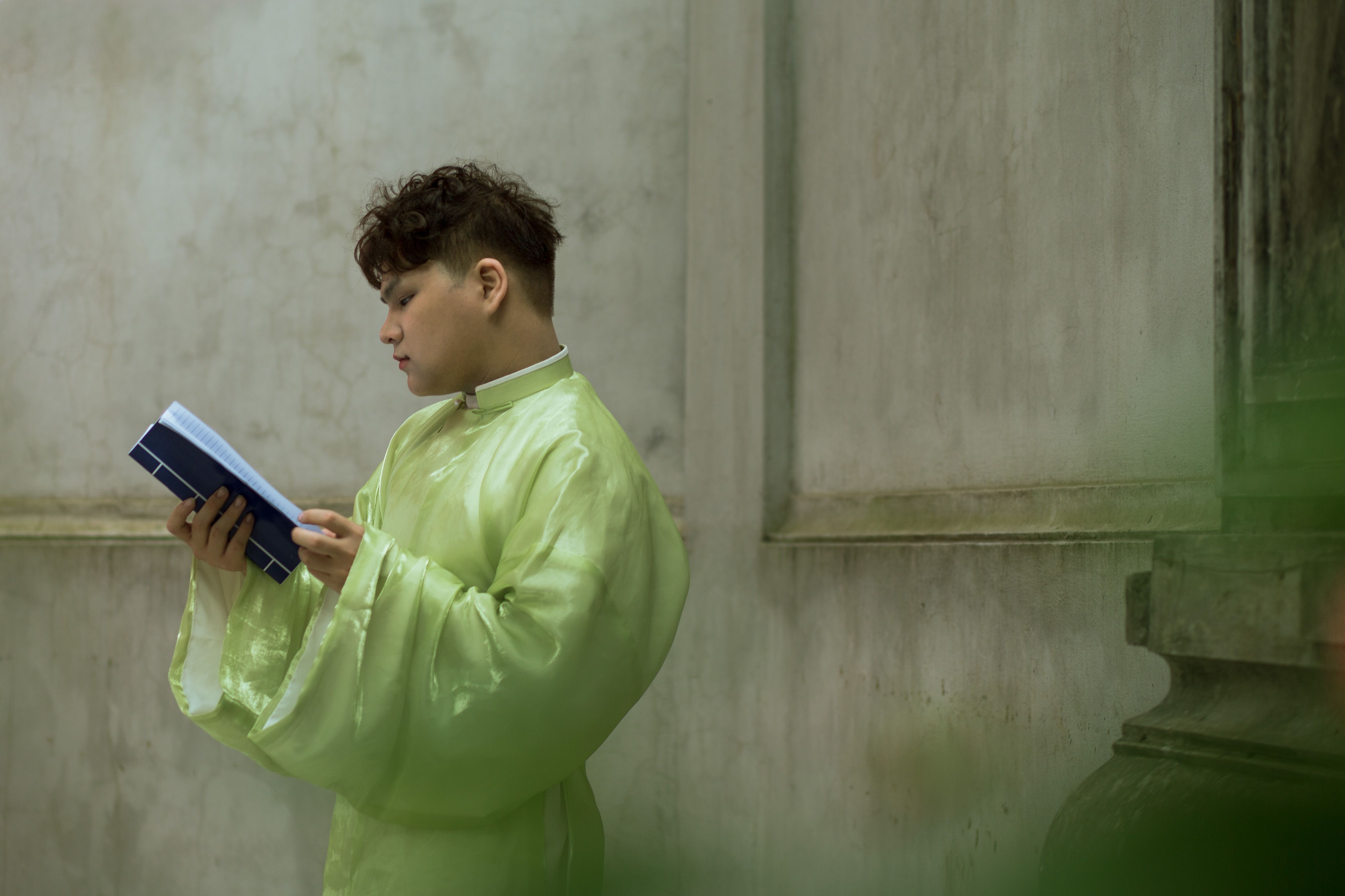 A man in traditional clothing reads attentively in a serene indoor setting.