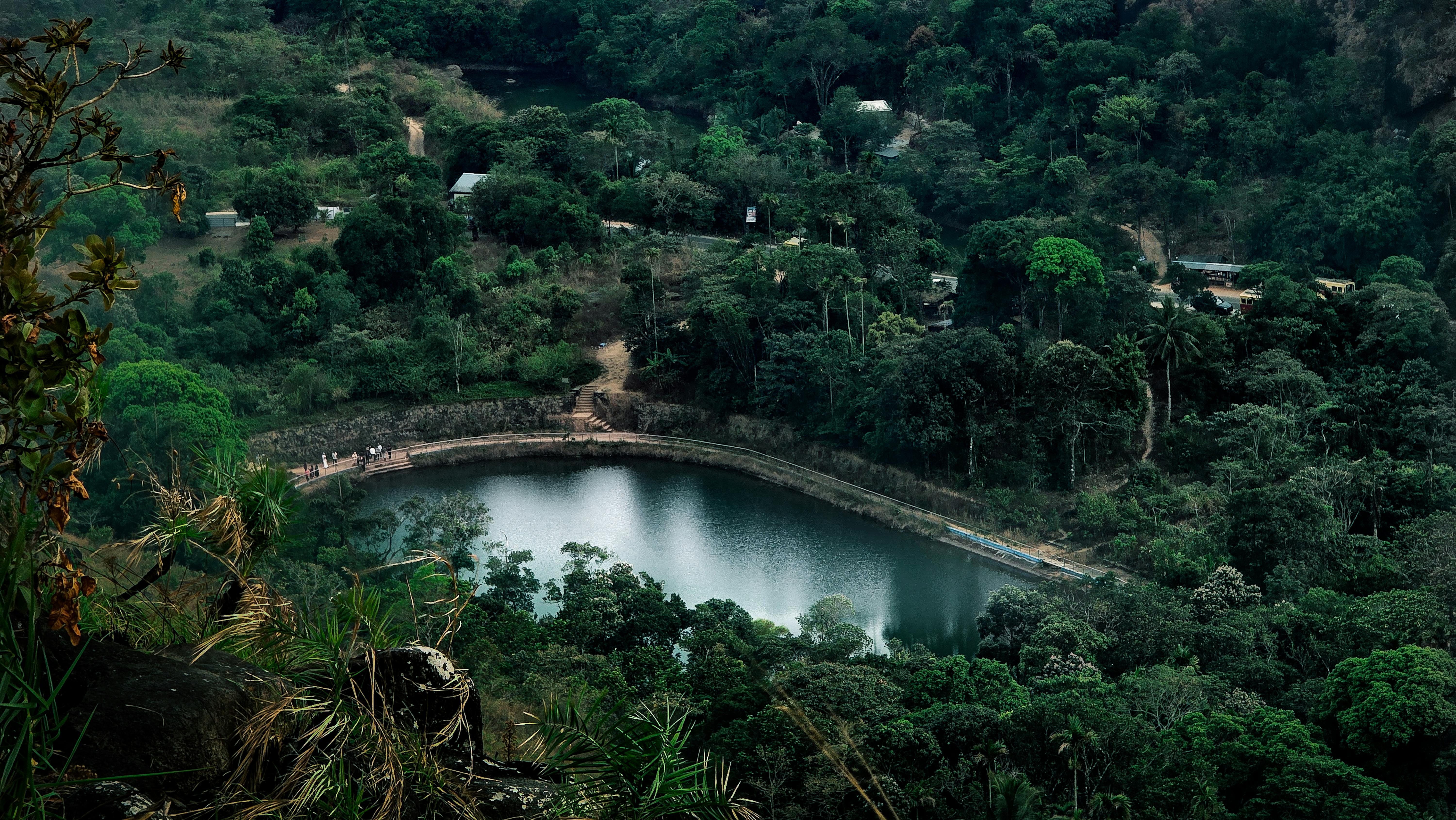 ฟรี ภาพถ่ายทางอากาศของป่าเขียวชอุ่มที่มีทะเลสาบเงียบสงบ ล้อมรอบด้วยต้นไม้หนาแน่นและสิ่งปลูกสร้างขนาดเล็ก คลังภาพถ่าย