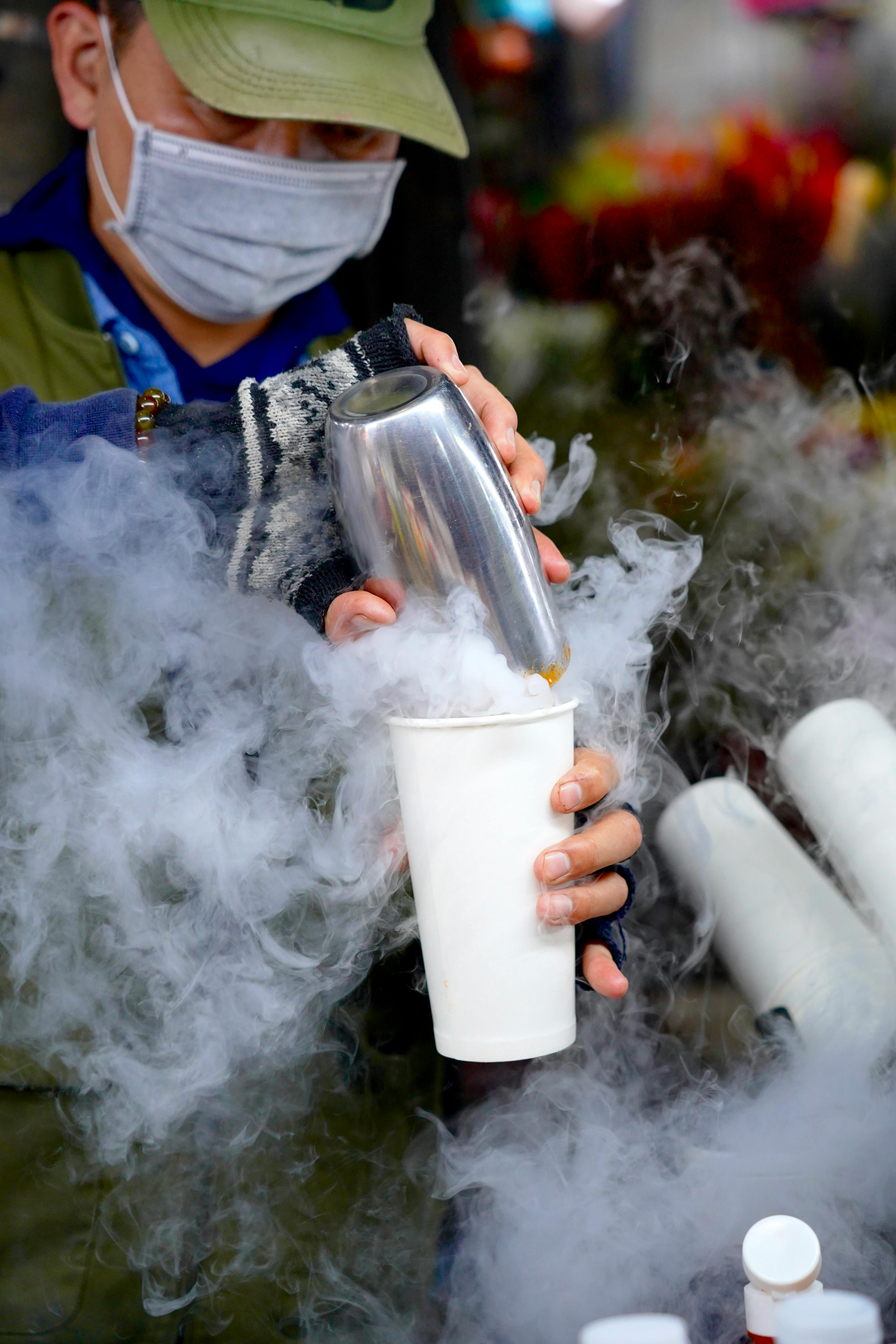 ฟรี บาริสต้าสวมหน้ากากกำลังเทของเหลวร้อนลงในถ้วยในบรรยากาศตลาดกลางแจ้ง คลังภาพถ่าย