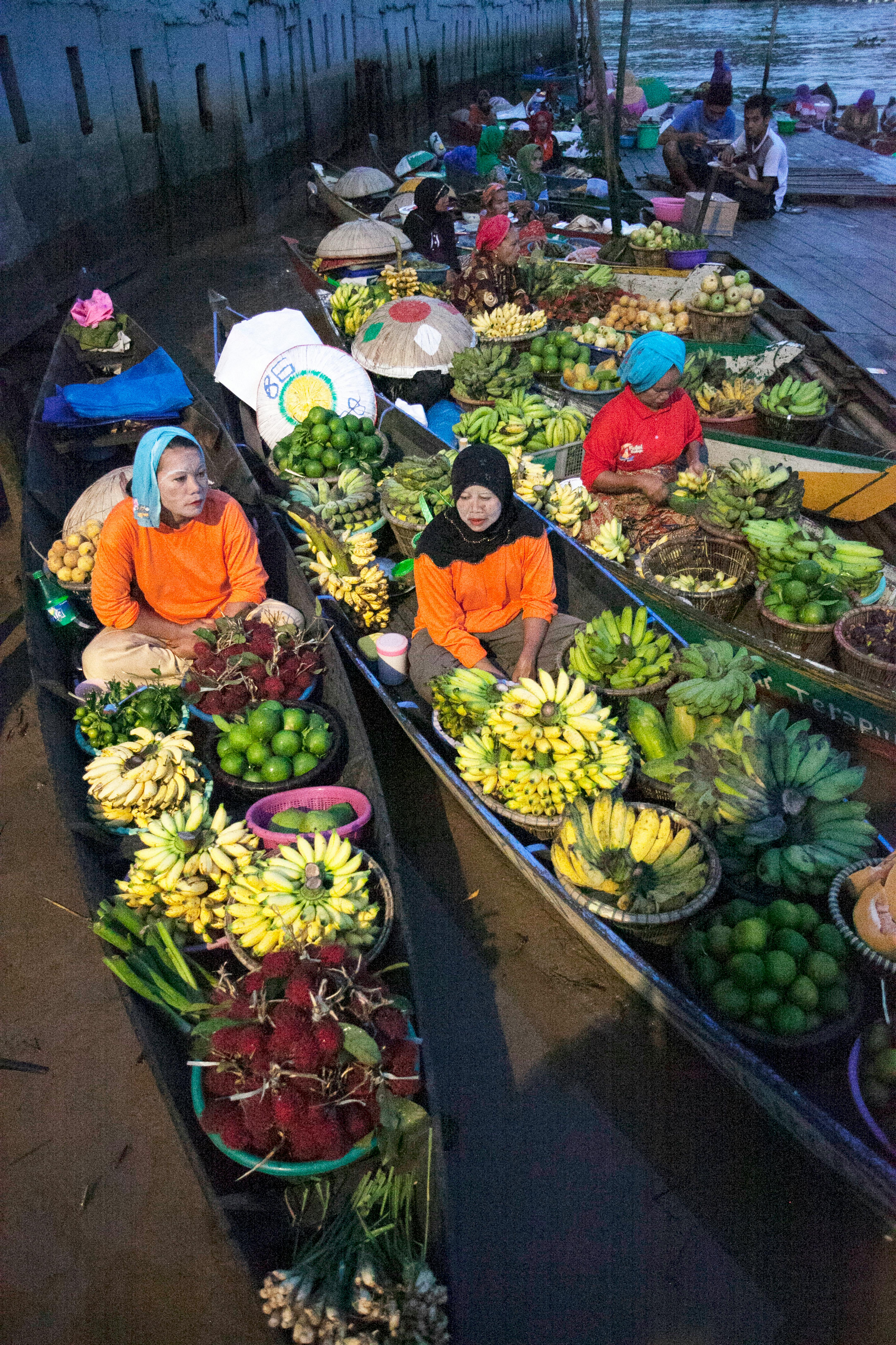 ฟรี ภาพบรรยากาศตลาดน้ำที่คึกคัก มีพ่อค้าแม่ค้าขายผลไม้บนเรือ นำกล้วย มะนาว และผลไม้อื่นๆ มาวางขาย คลังภาพถ่าย