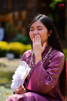 Portrait of a young woman in traditional clothing holding a fan outdoors, smiling gently.