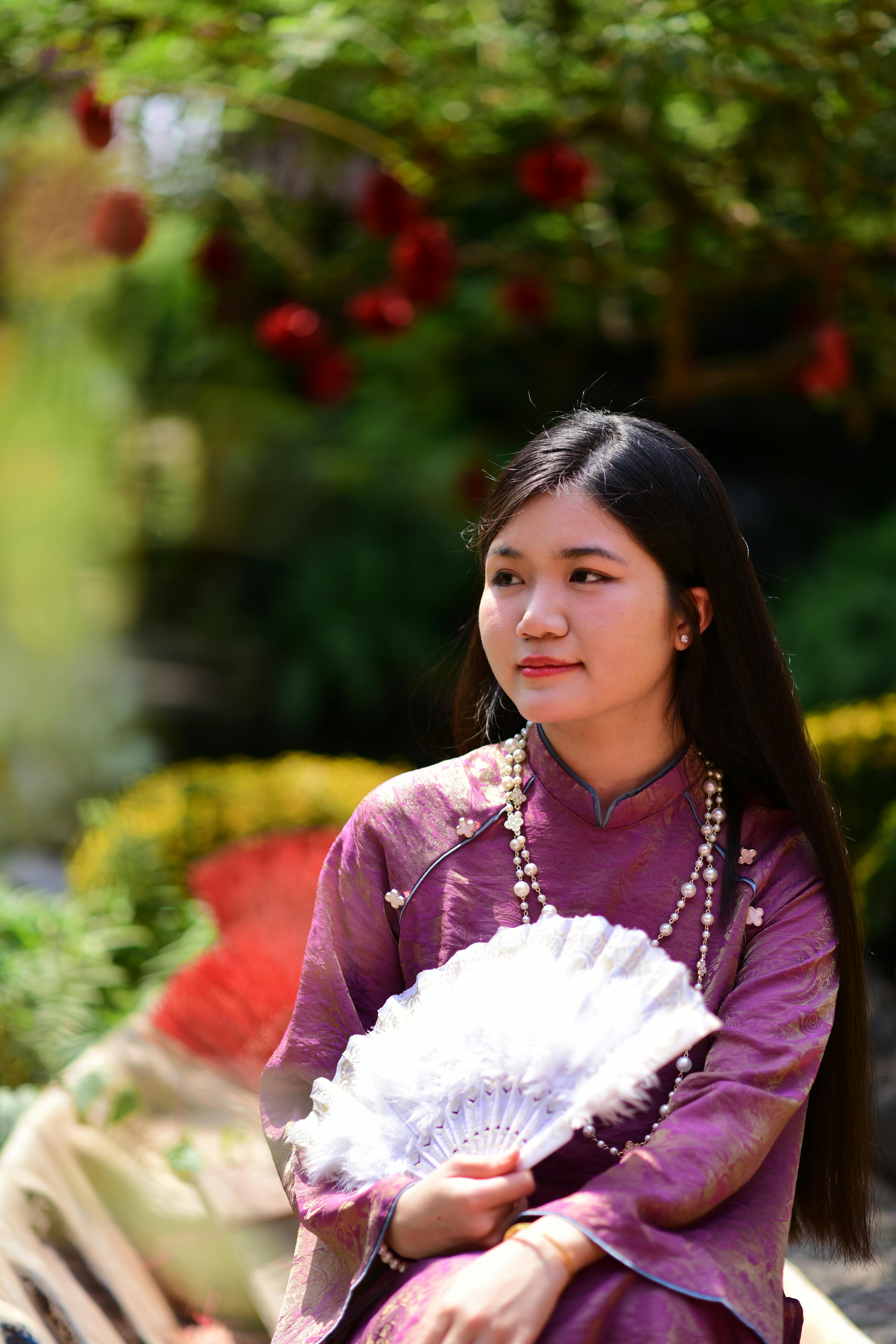 Free Portrait of a young woman in traditional attire, holding a fan outdoors amidst nature. Stock Photo