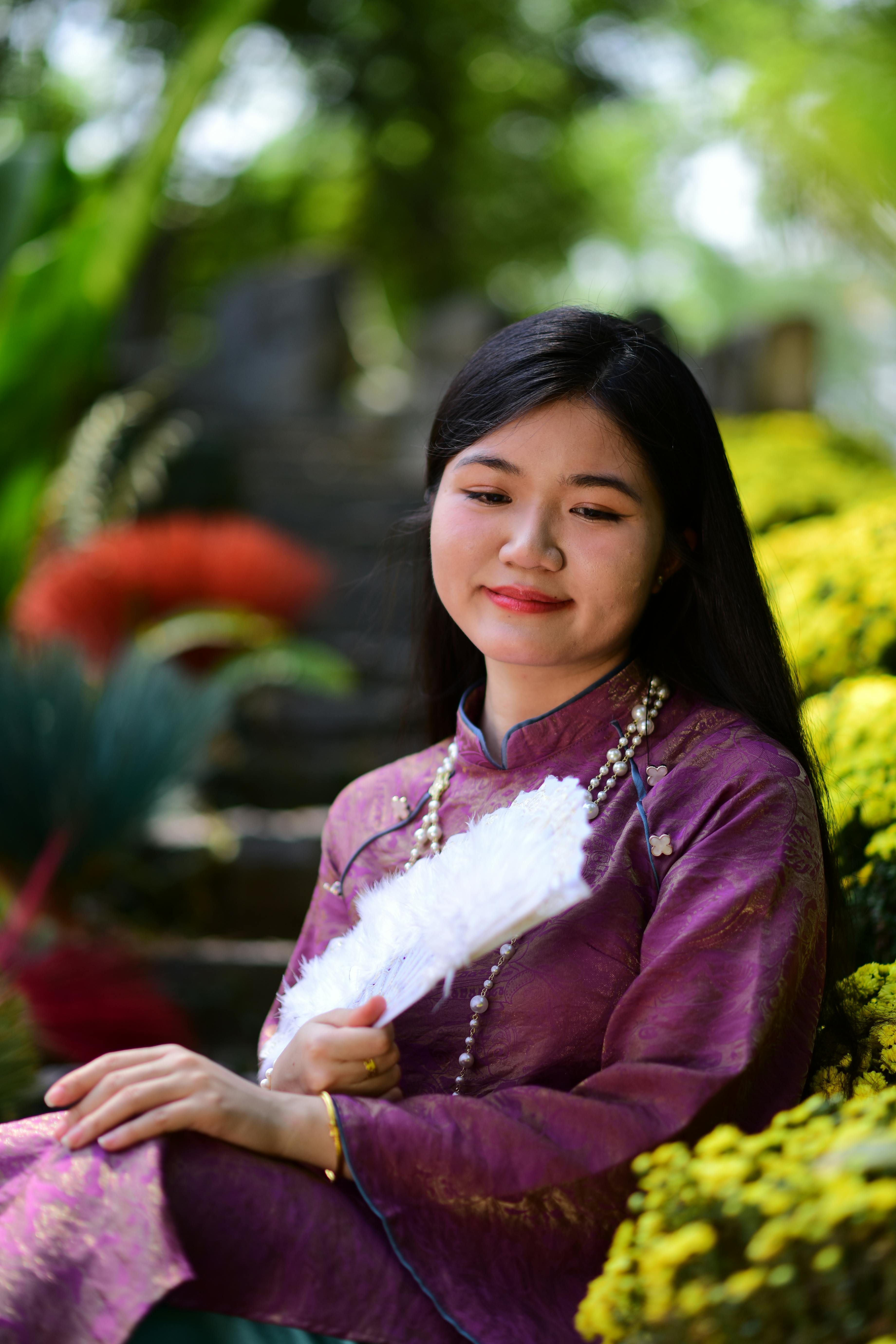Free Asian woman in traditional dress relaxing in vibrant outdoor garden. Stock Photo