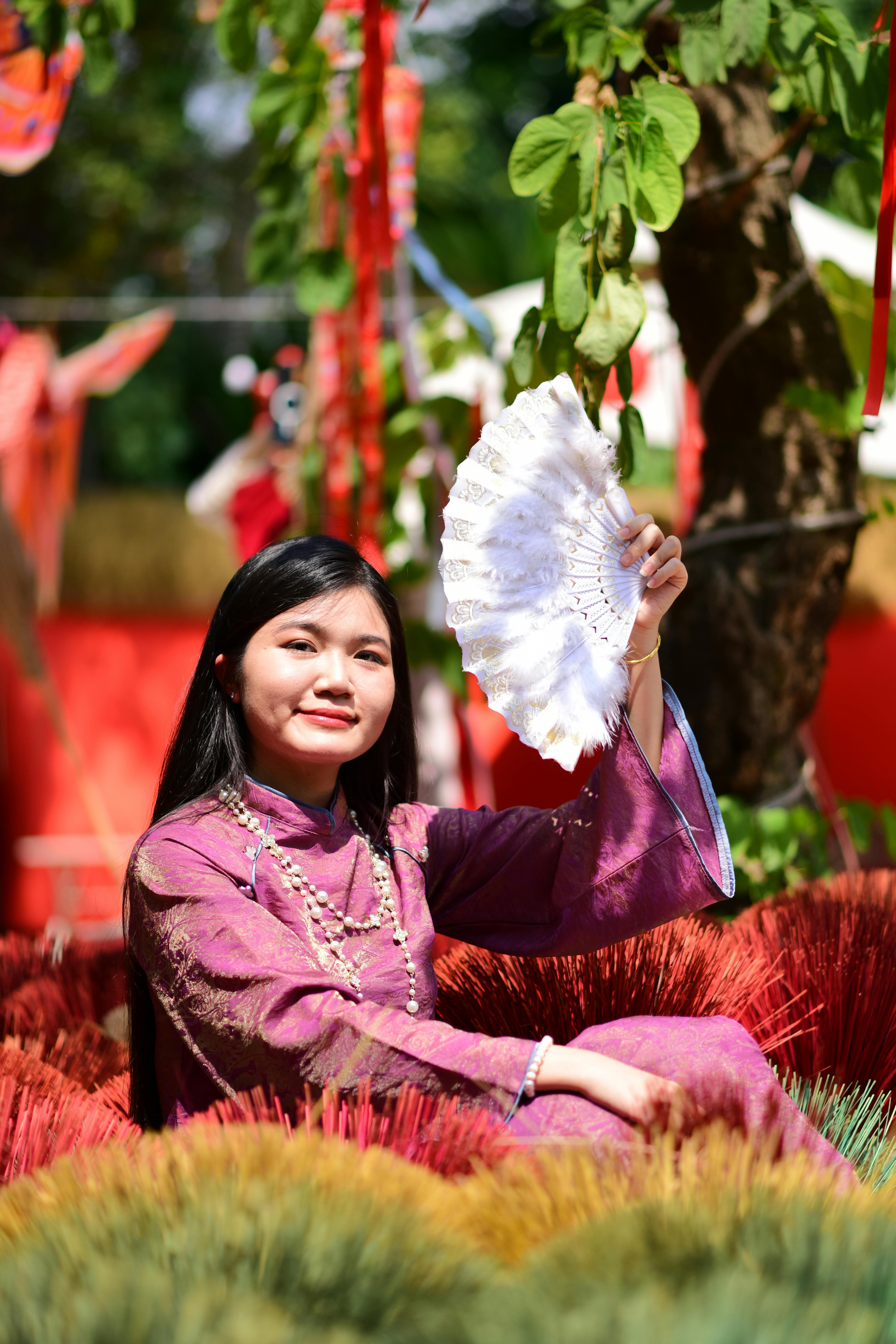 Gratis Ritratto di una donna in abiti tradizionali che tiene in mano un ventaglio e si gode un soleggiato paesaggio all'aperto. Foto a disposizione