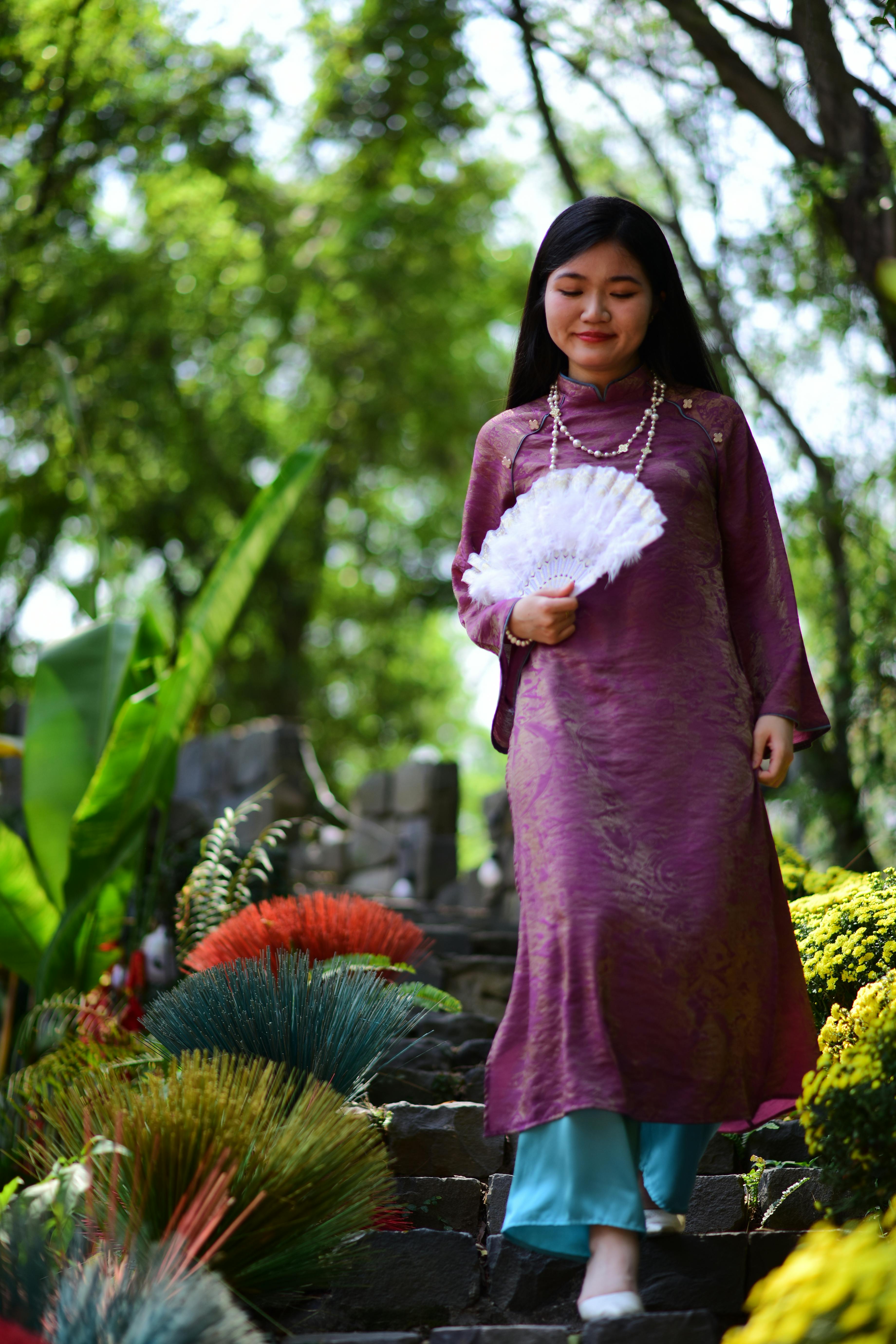 Gratis Donna in abito tradizionale viola che scende i gradini di pietra circondata da piante rigogliose. Foto a disposizione