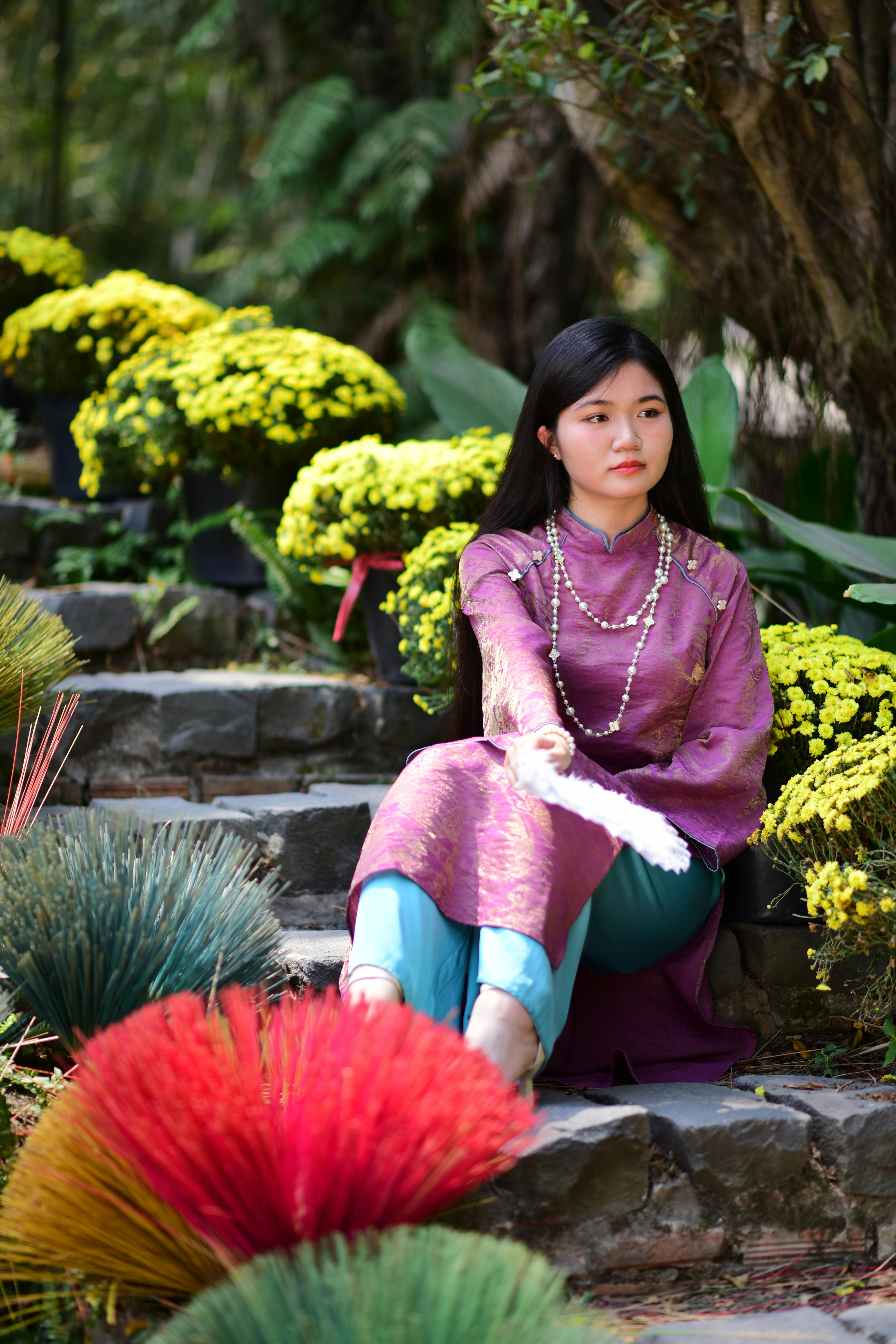 Ilmainen Perinteisessä asussa oleva nainen istuu kiviportailla värikkäiden kasvien ja kukkien ympäröimänä. Kuvapankkikuva