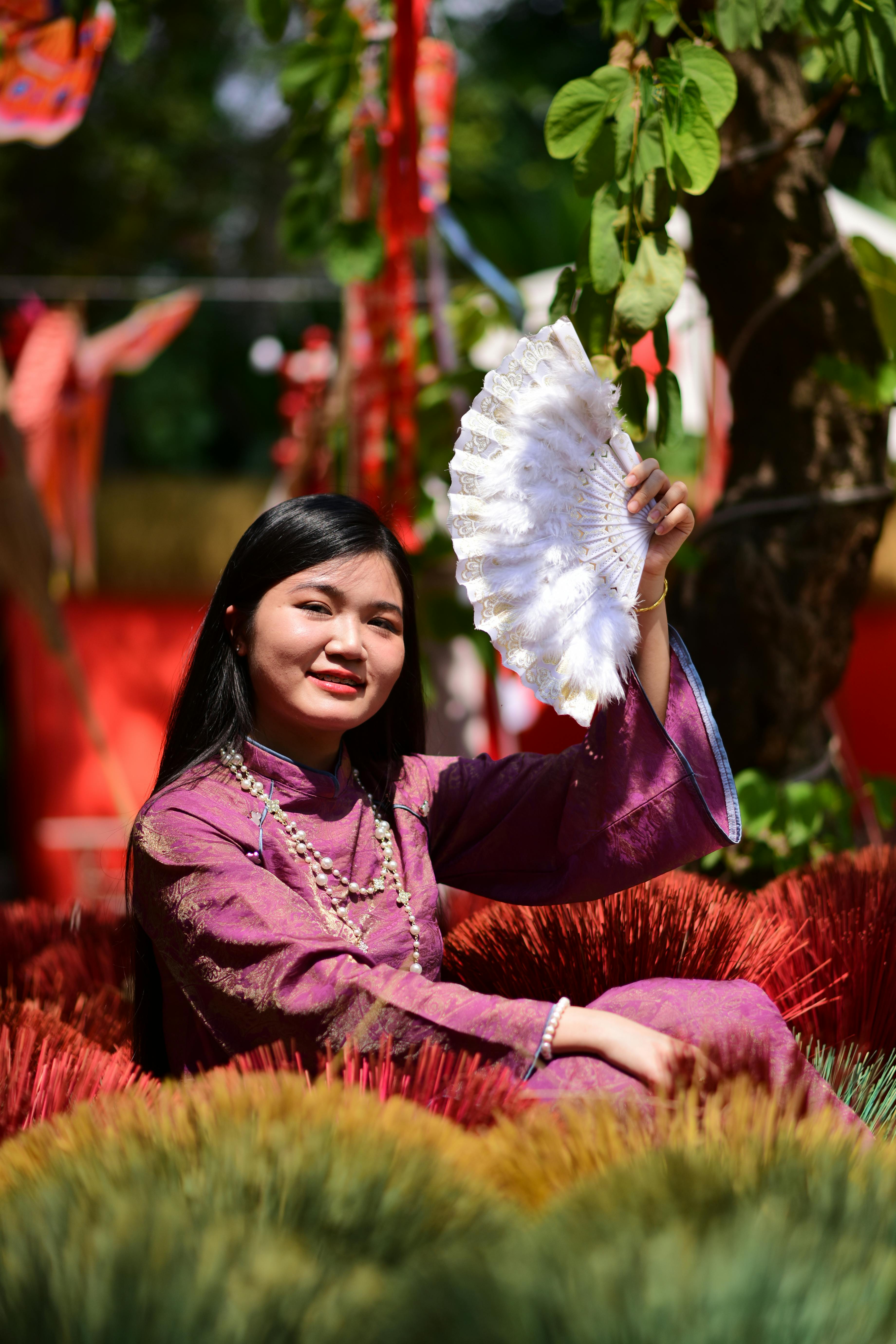 ฟรี หญิงชาวเอเชียในชุดพื้นเมืองสีม่วงกำลังยิ้มและถือพัด คลังภาพถ่าย