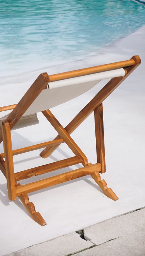 Free A relaxing wooden deck chair beside a clear blue swimming pool, ideal for a summer day. Stock Photo
