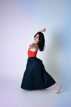 A dancer captures a graceful pose in a studio. Red top contrasts beautifully with her flowing dark skirt.