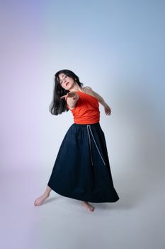 A woman in an orange top and black skirt gracefully dancing in a studio setting.