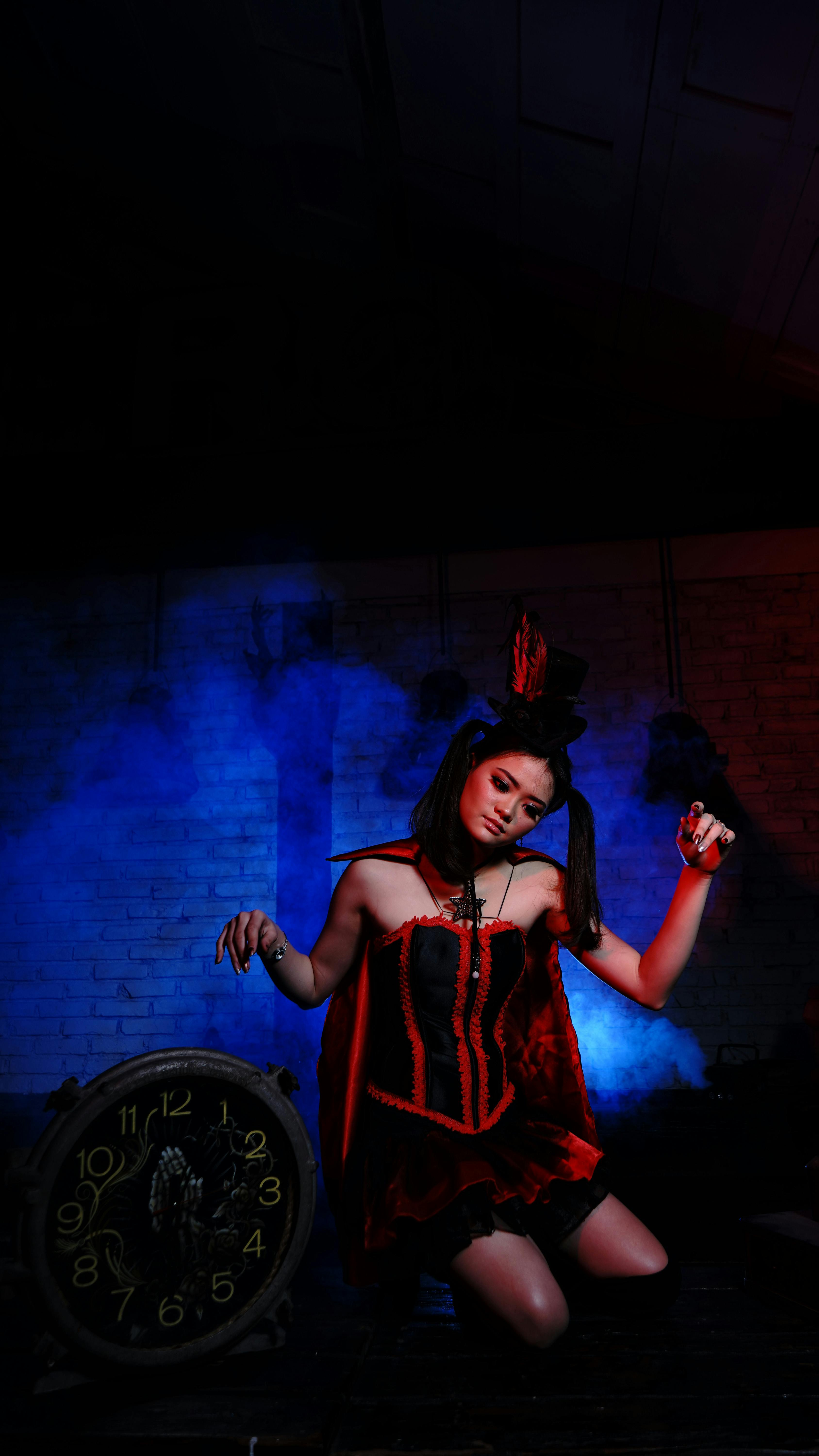 Free A woman in dramatic makeup and costume posing with a vintage clock under moody lighting. Stock Photo