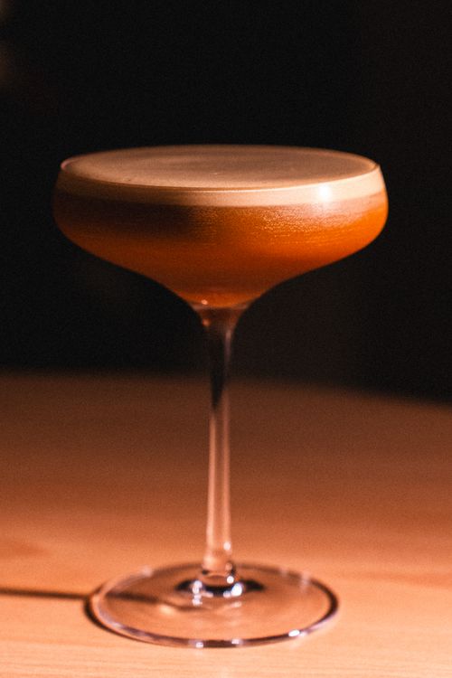 Free Close-up of an elegant cocktail with foam served in a coupe glass in a dimly lit setting. Stock Photo