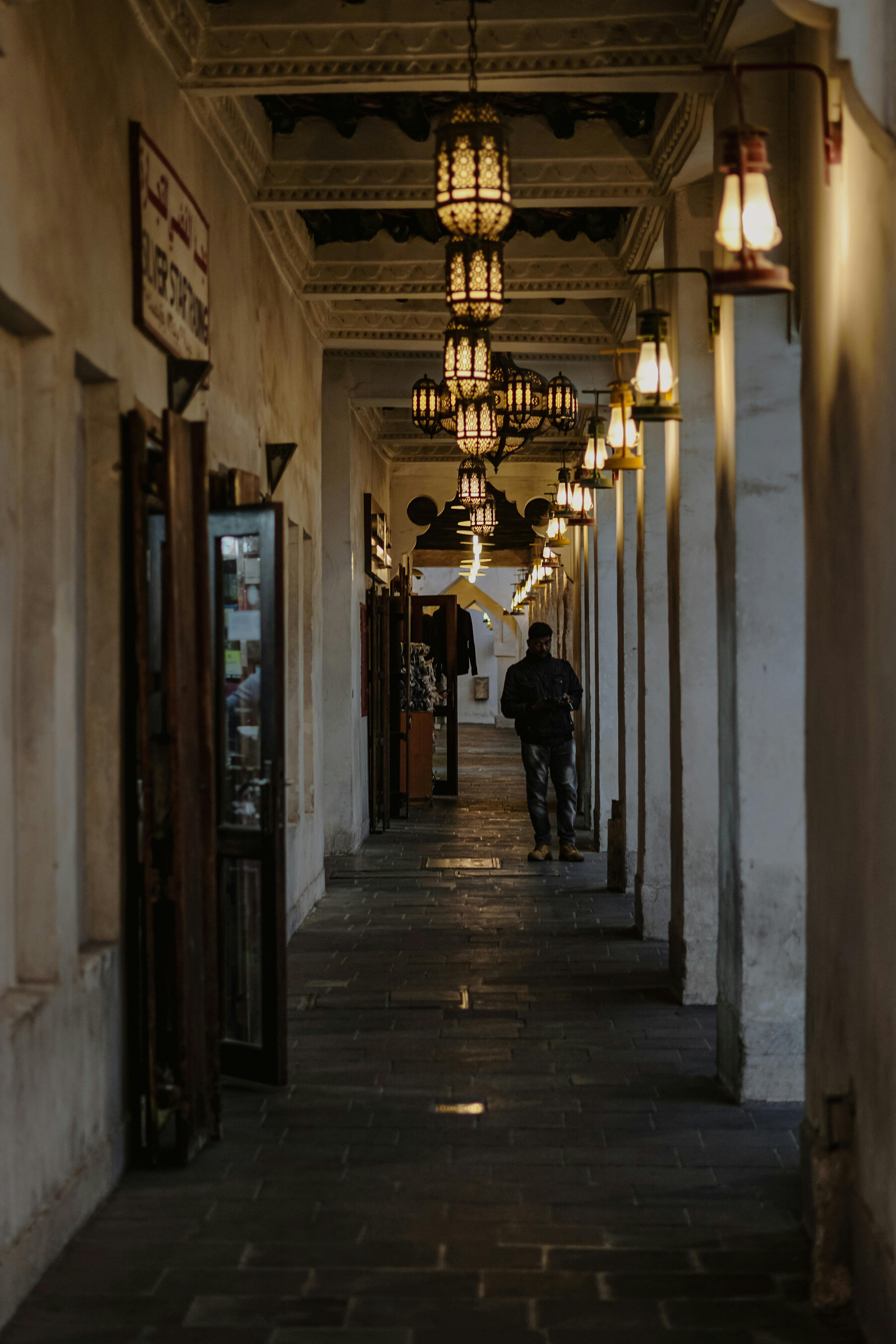 Gratis Un pasillo poco iluminado con linternas tradicionales y una persona caminando en Souq Waqif, Qatar. Foto de stock