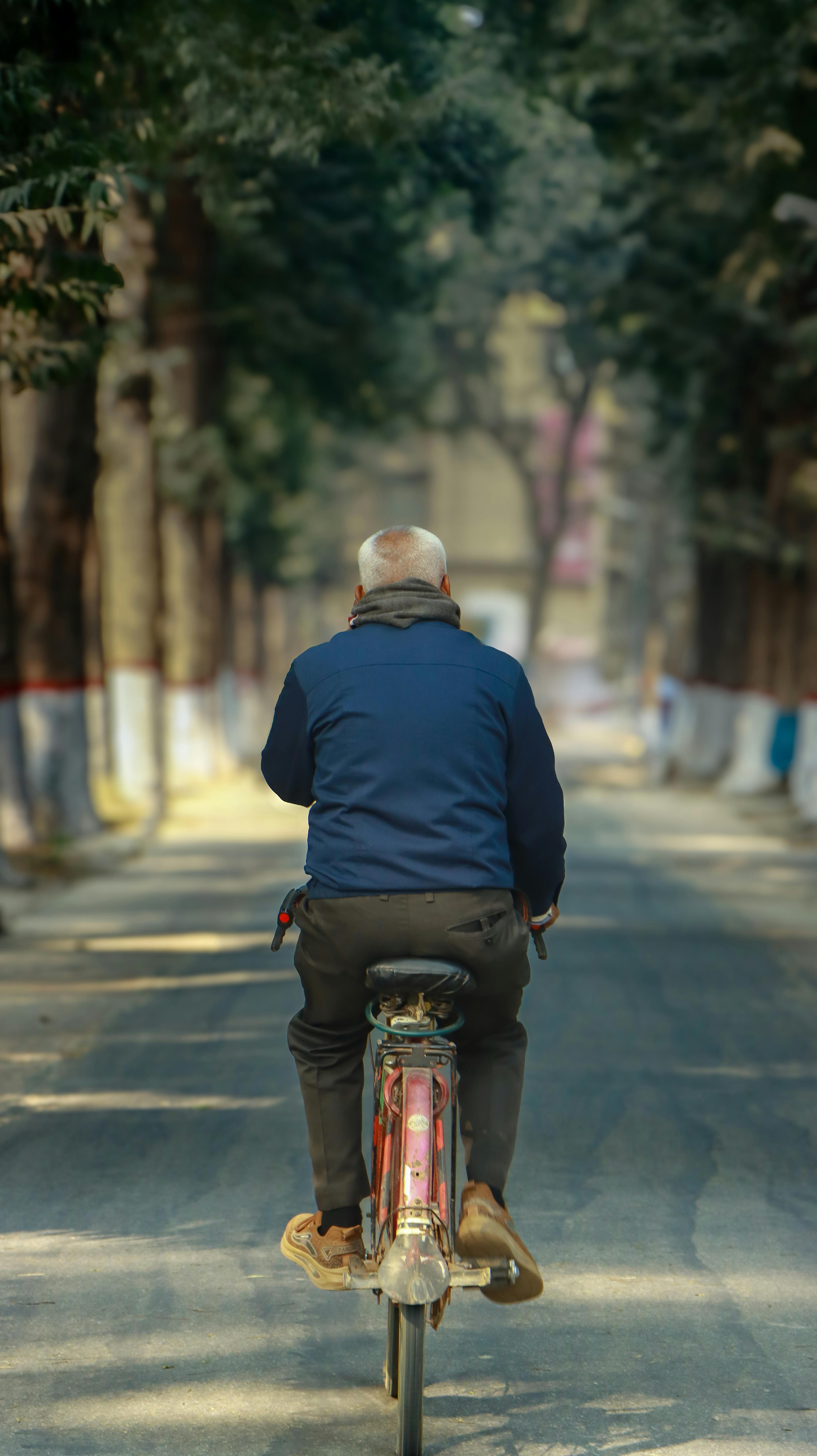 Ilmainen Vanhempi mies pyöräilee puiden reunustamalla kadulla Bangladeshissa osoittaen rauhallisuutta ja aktiivista elämäntapaa. Kuvapankkikuva