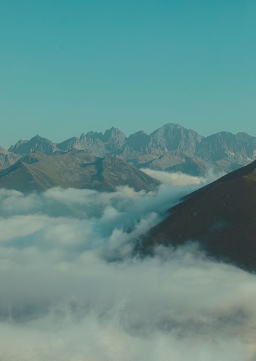 Free A serene view of mountains emerging through a sea of clouds under a clear blue sky. Stock Photo
