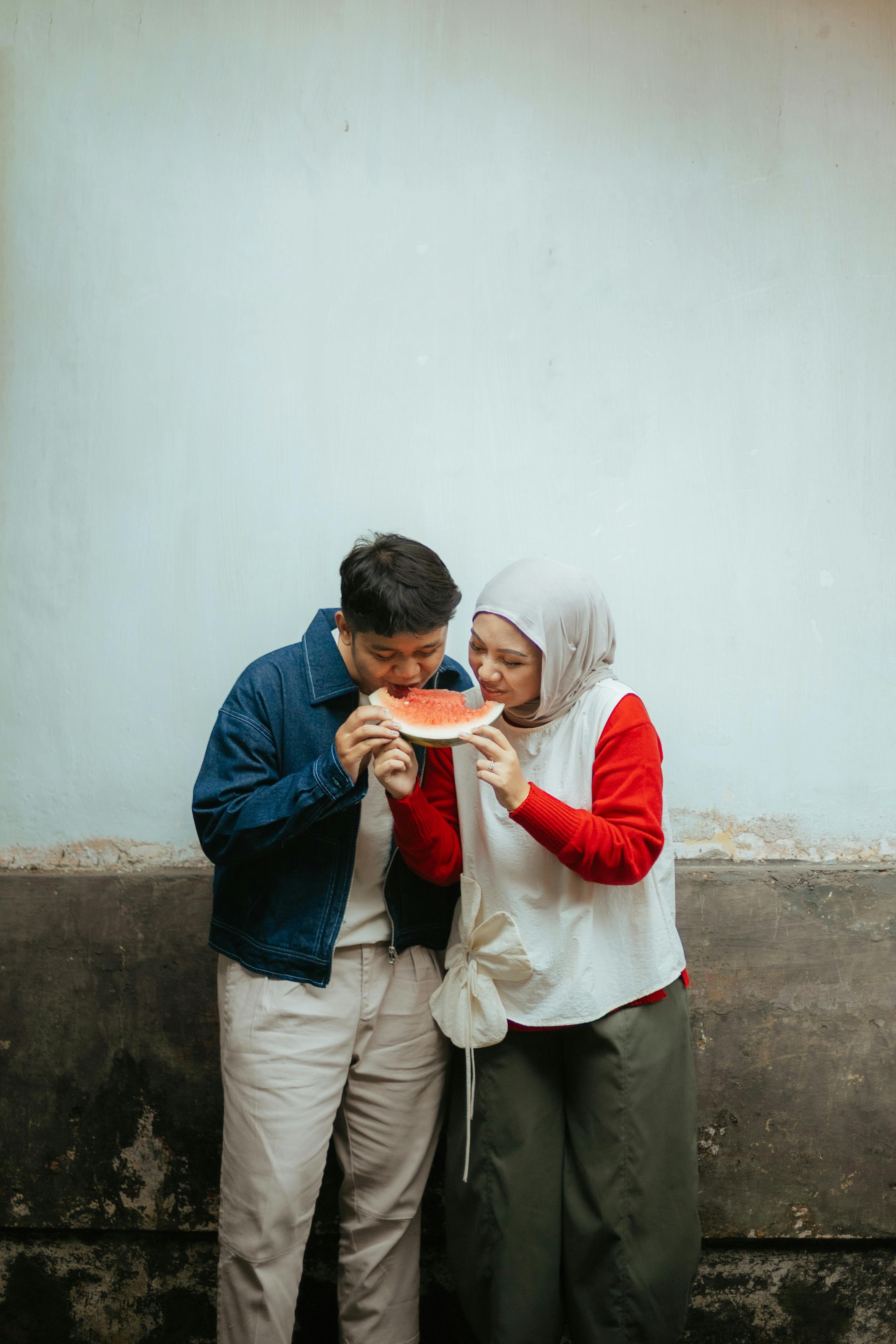 Ilmainen Onnellinen pariskunta rennossa asussa jakavat vesimelonia ulkona Indonesiassa. Kuvapankkikuva