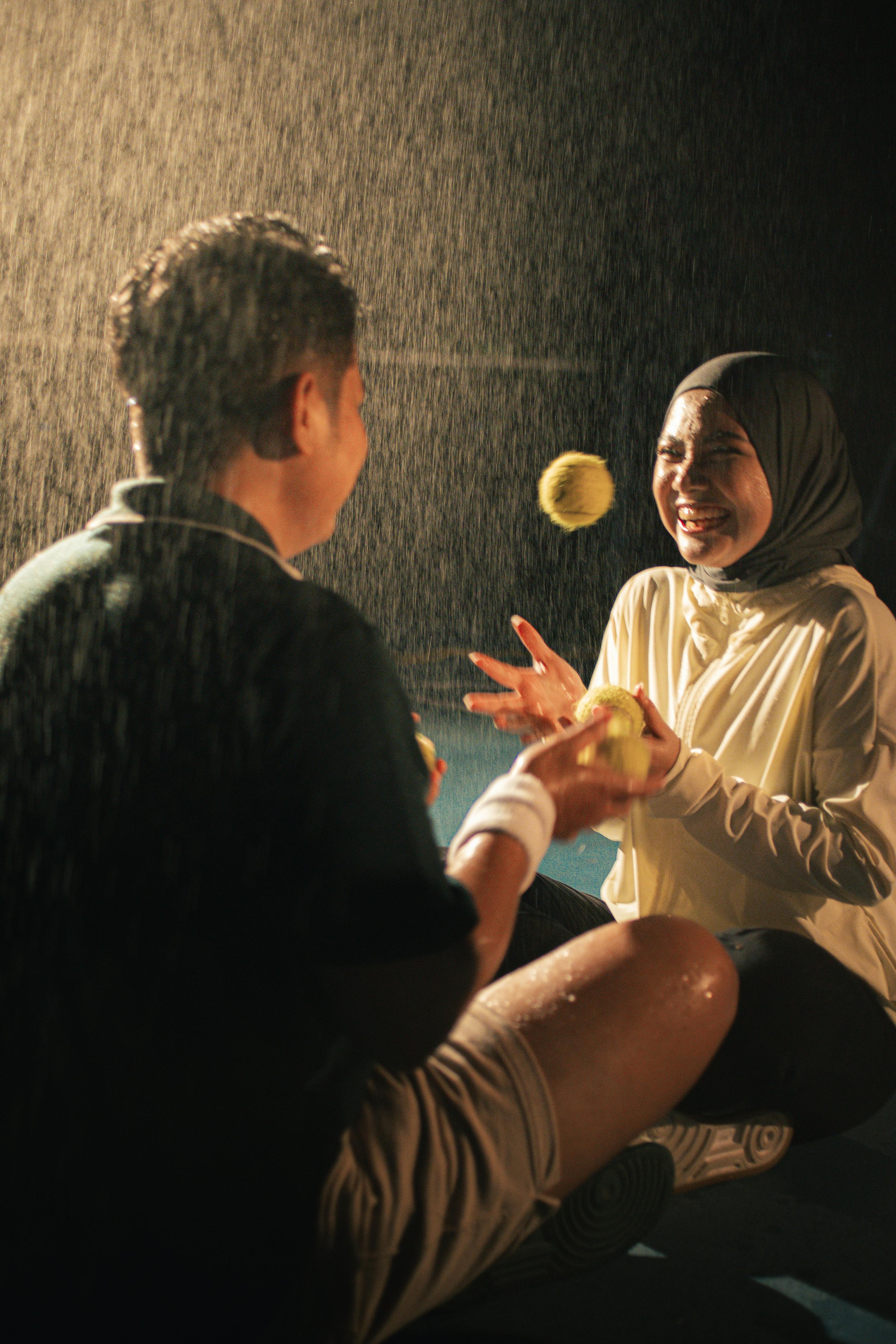 Free Couple enjoying a playful moment with tennis balls, drenched in rain. Stock Photo