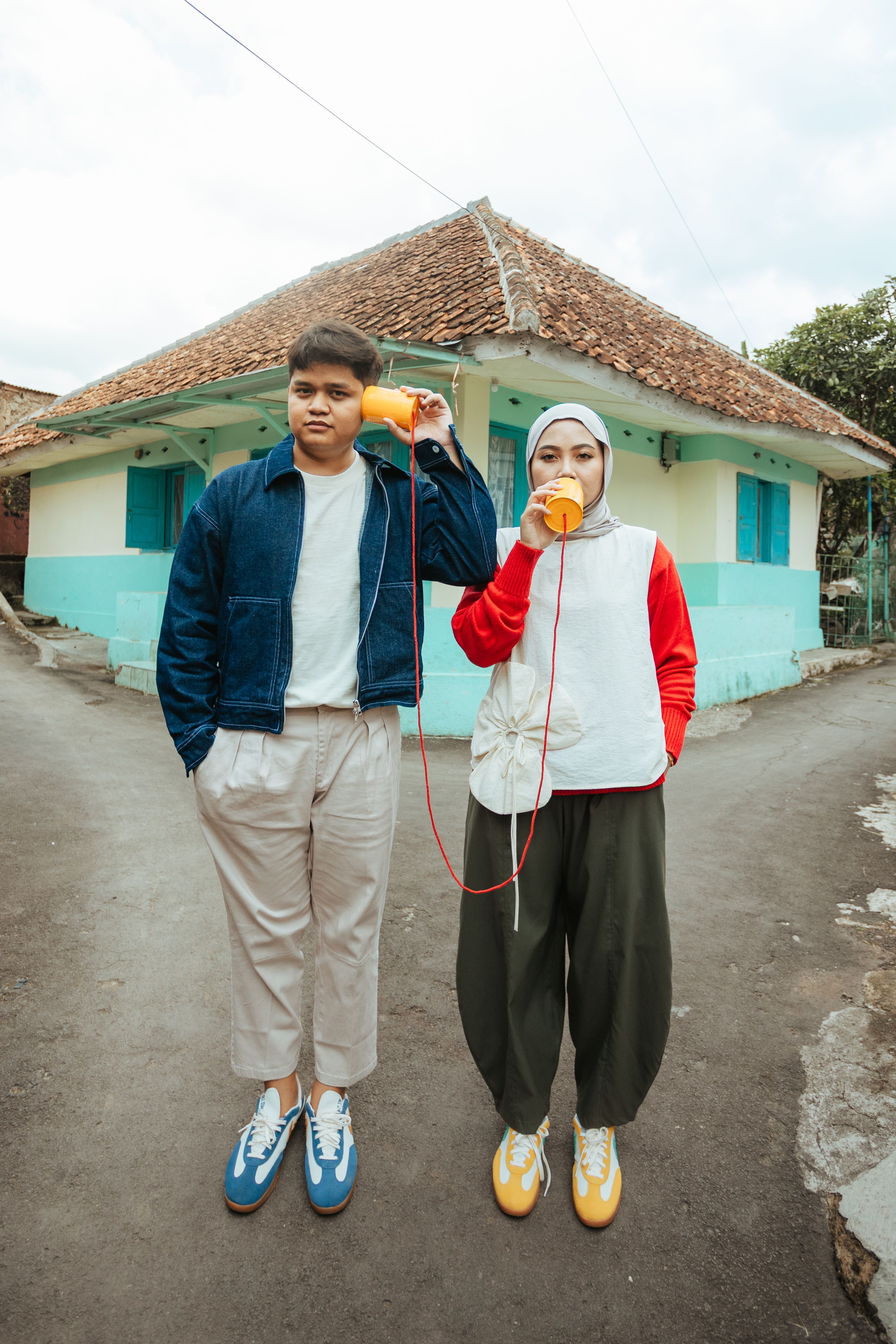 A young Asian couple using tin can phones in a quaint street in Indonesia. Vibrant and playful.