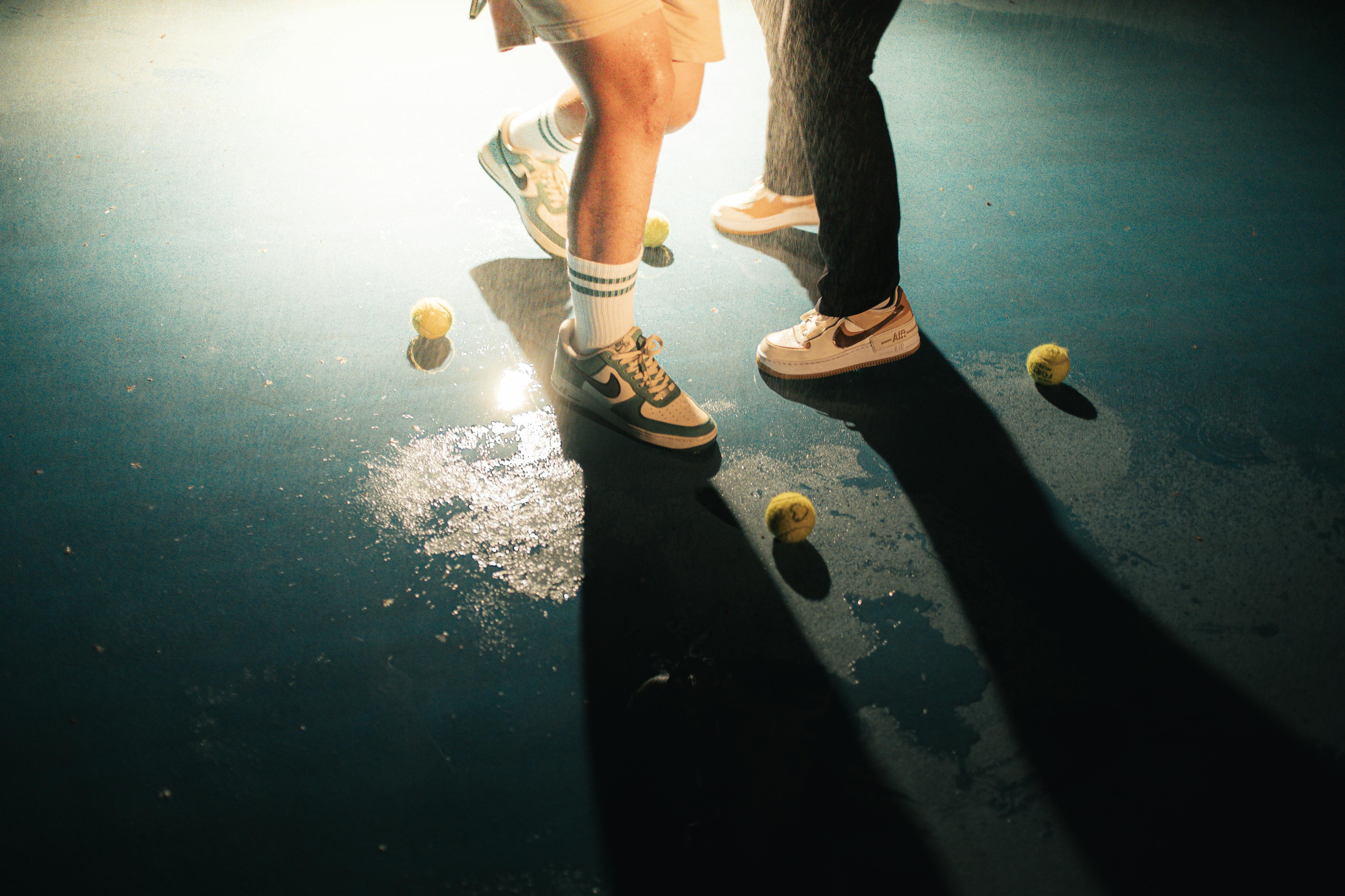Free Close-up of tennis shoes and balls on wet court with dramatic lighting. Stock Photo