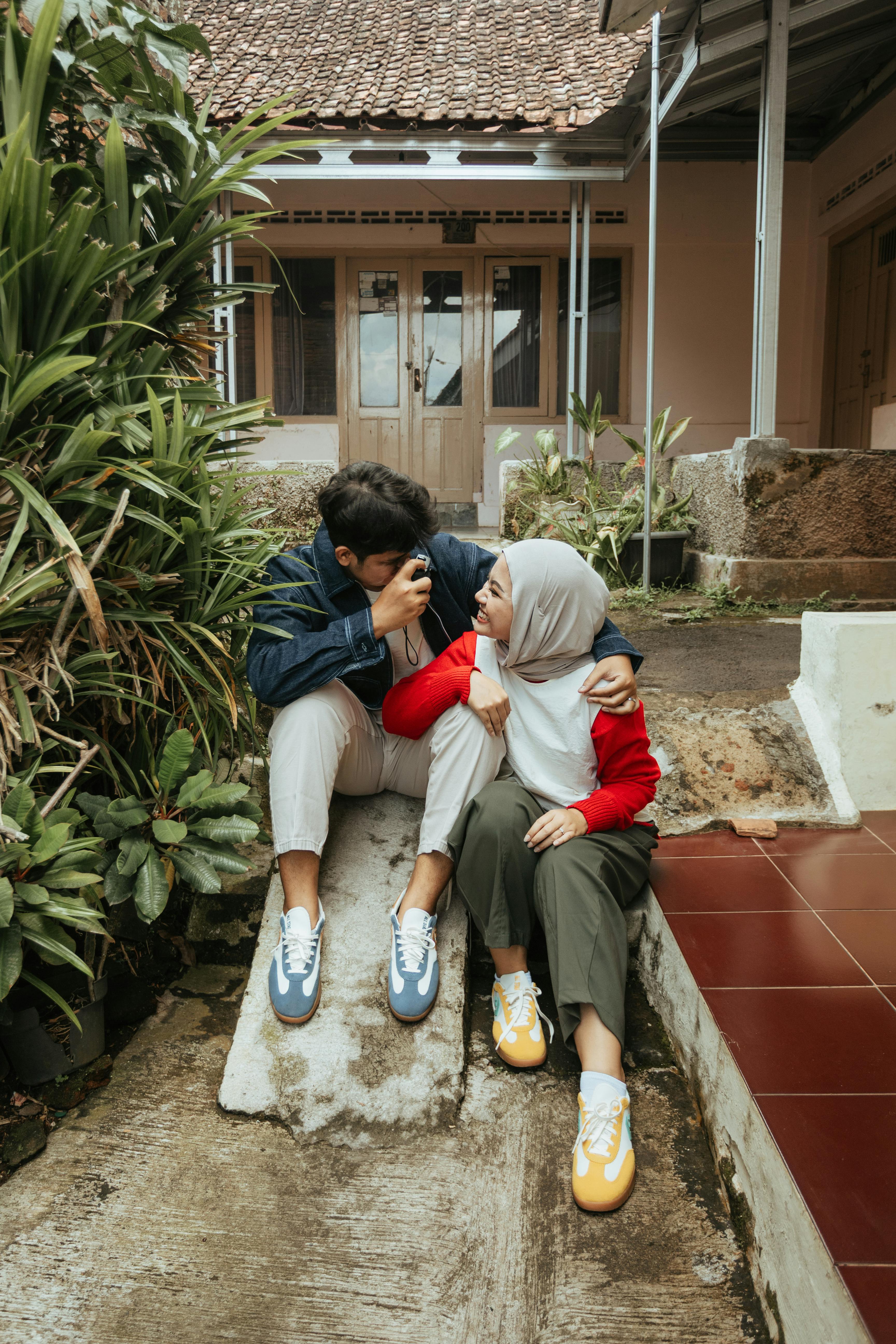 ฟรี คู่รักหนุ่มสาวกำลังเพลิดเพลินกับช่วงเวลาพักผ่อนด้วยกันในลานบ้านสไตล์อินโดนีเซียที่สวยงาม คลังภาพถ่าย