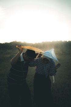 An engaged couple in Indonesia enjoys a playful moment under umbrellas in a lush countryside setting.
