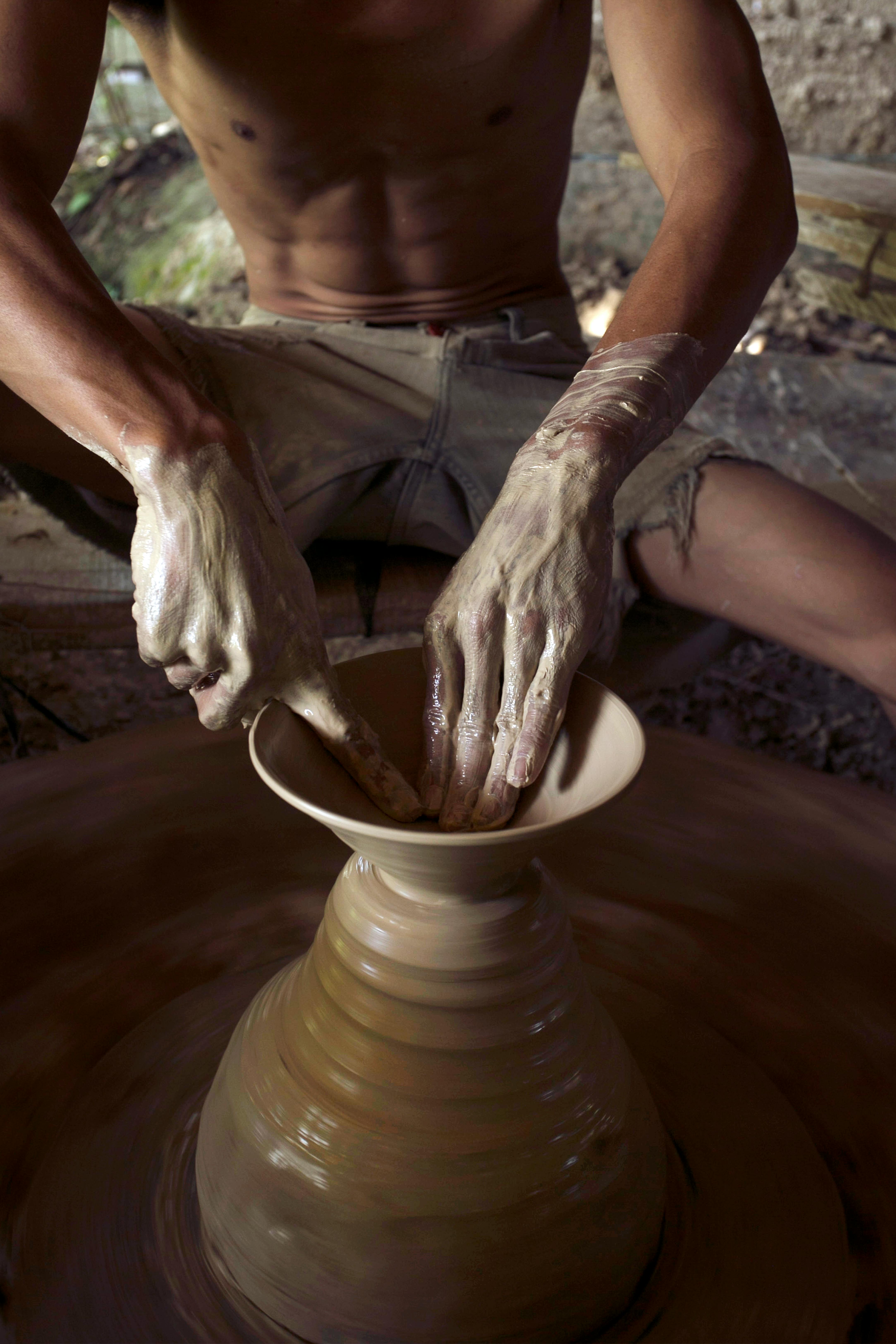 ฟรี ภาพระยะใกล้ของมือช่างปั้นดินเผาที่กำลังปั้นดินเหนียวอย่างชำนาญบนวงล้อหมุนภายในอาคาร คลังภาพถ่าย