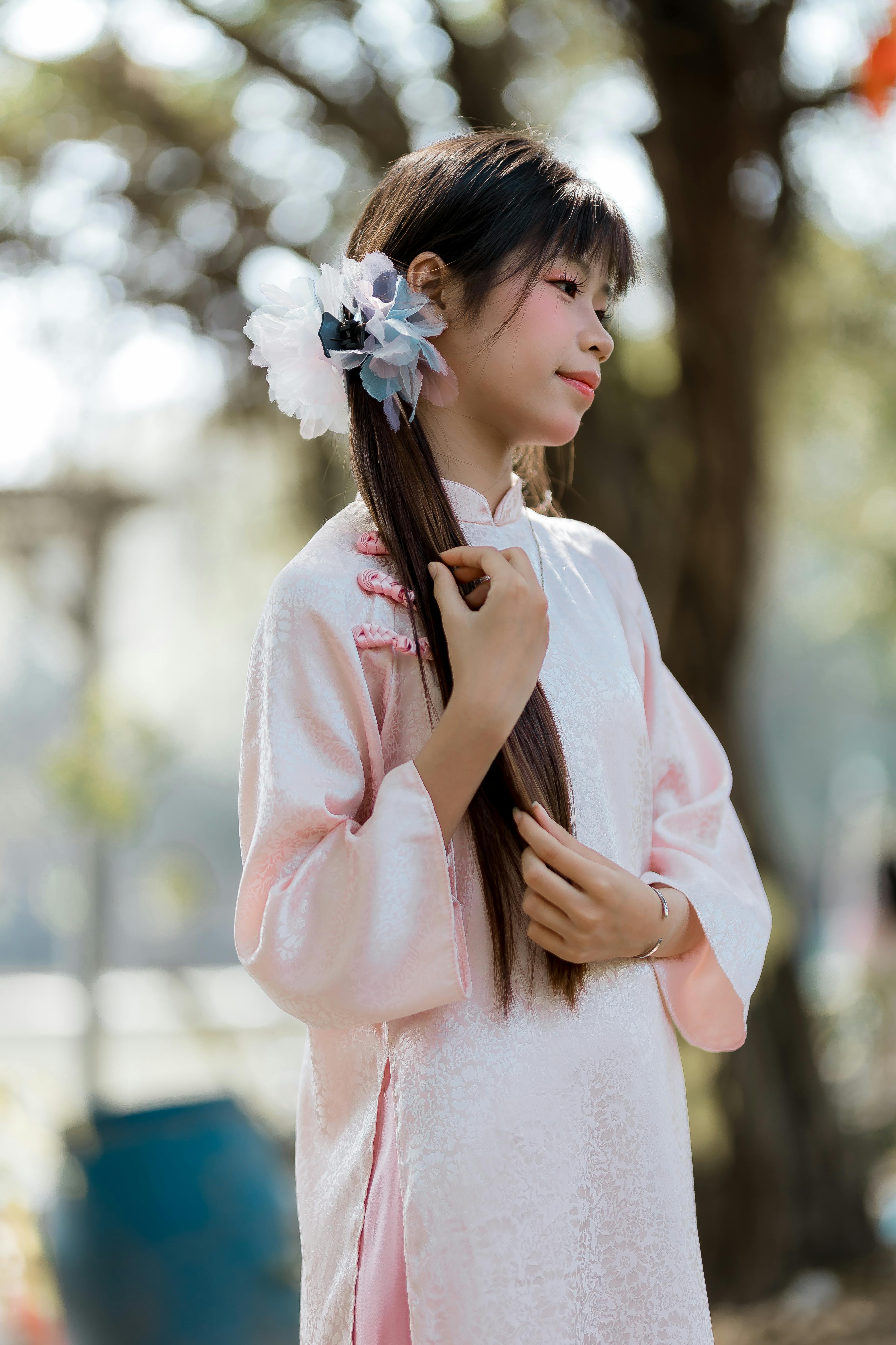 Ilmainen Nuori nainen kauniissa vaaleanpunaisessa perinteisessä mekossa ja kukkakuvioisessa hiusasusteessa rauhallisessa ulkoilmaympäristössä. Kuvapankkikuva