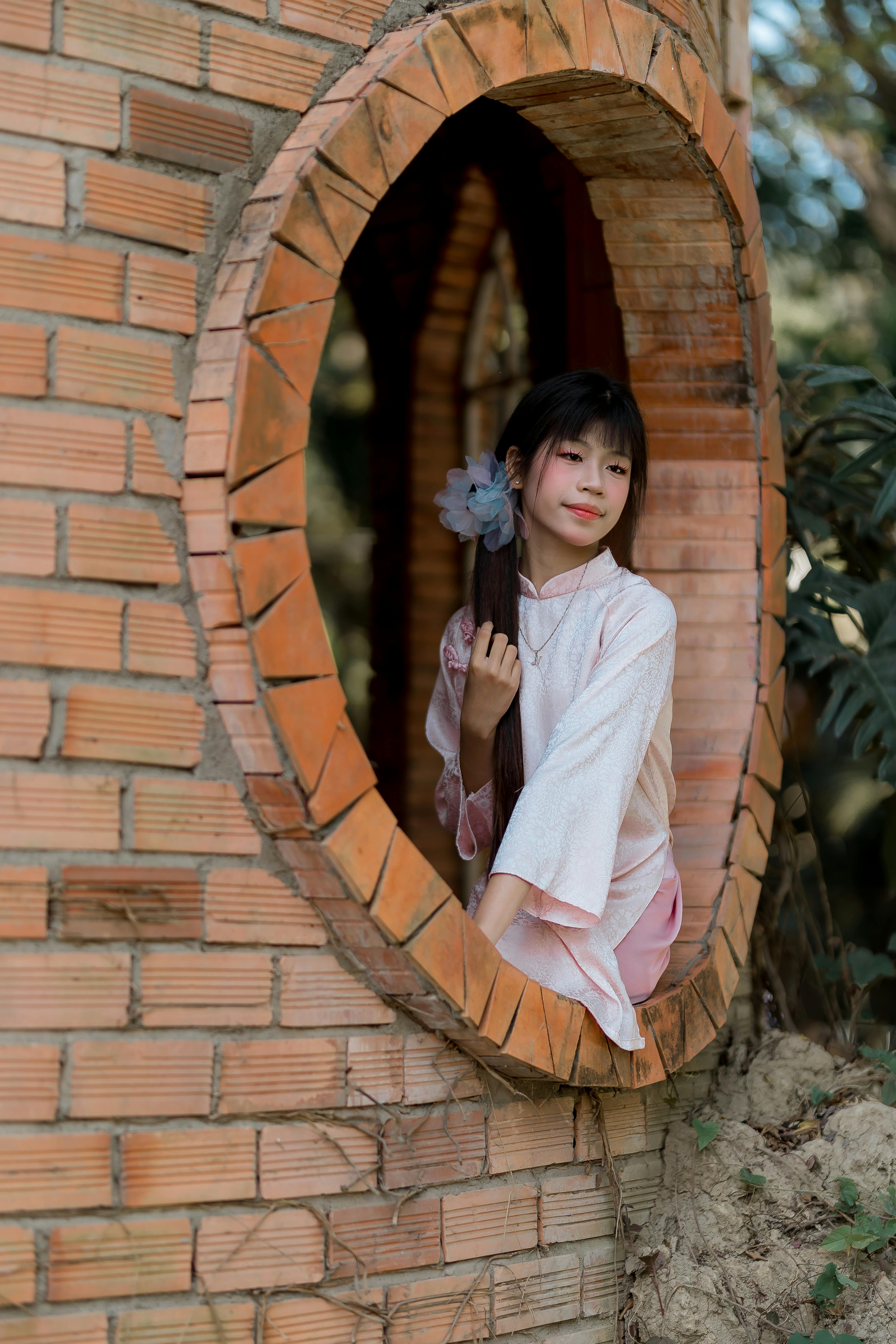 bezplatná Žena v růžovém tradičním oblečení sedí venku v kruhovém cihlovém okně. Základová fotografie