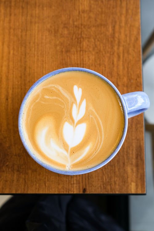 Free A close-up top view of a latte with an intricate leaf pattern in a blue ceramic cup on a wooden table. Stock Photo