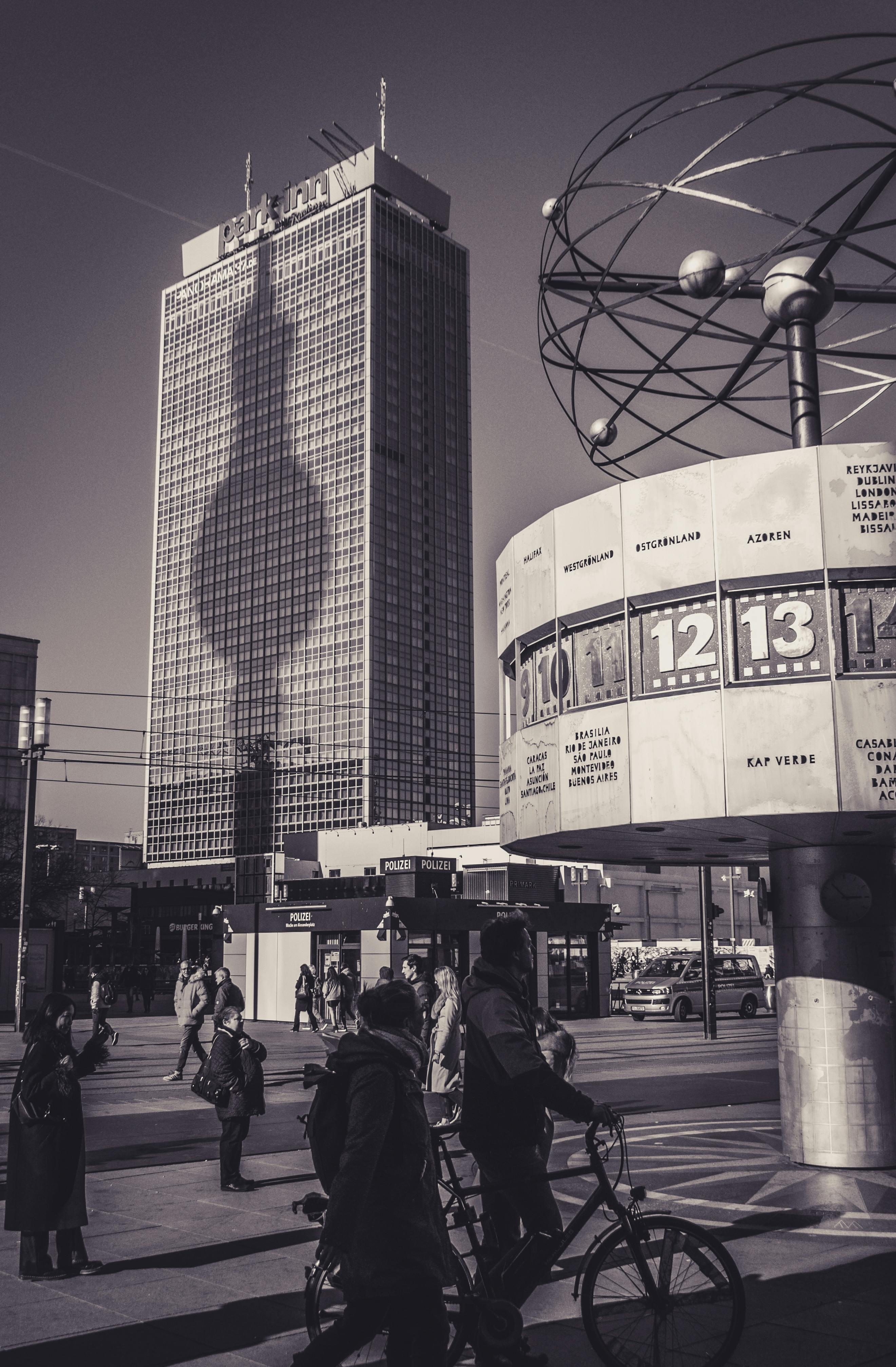 Gratuit Vue saisissante du paysage urbain de Berlin, avec un immeuble imposant projetant son ombre sur une place publique animée. Photos
