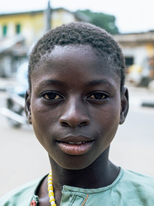 Free Close-up portrait of a young boy standing on a street with buildings in the background. Stock Photo