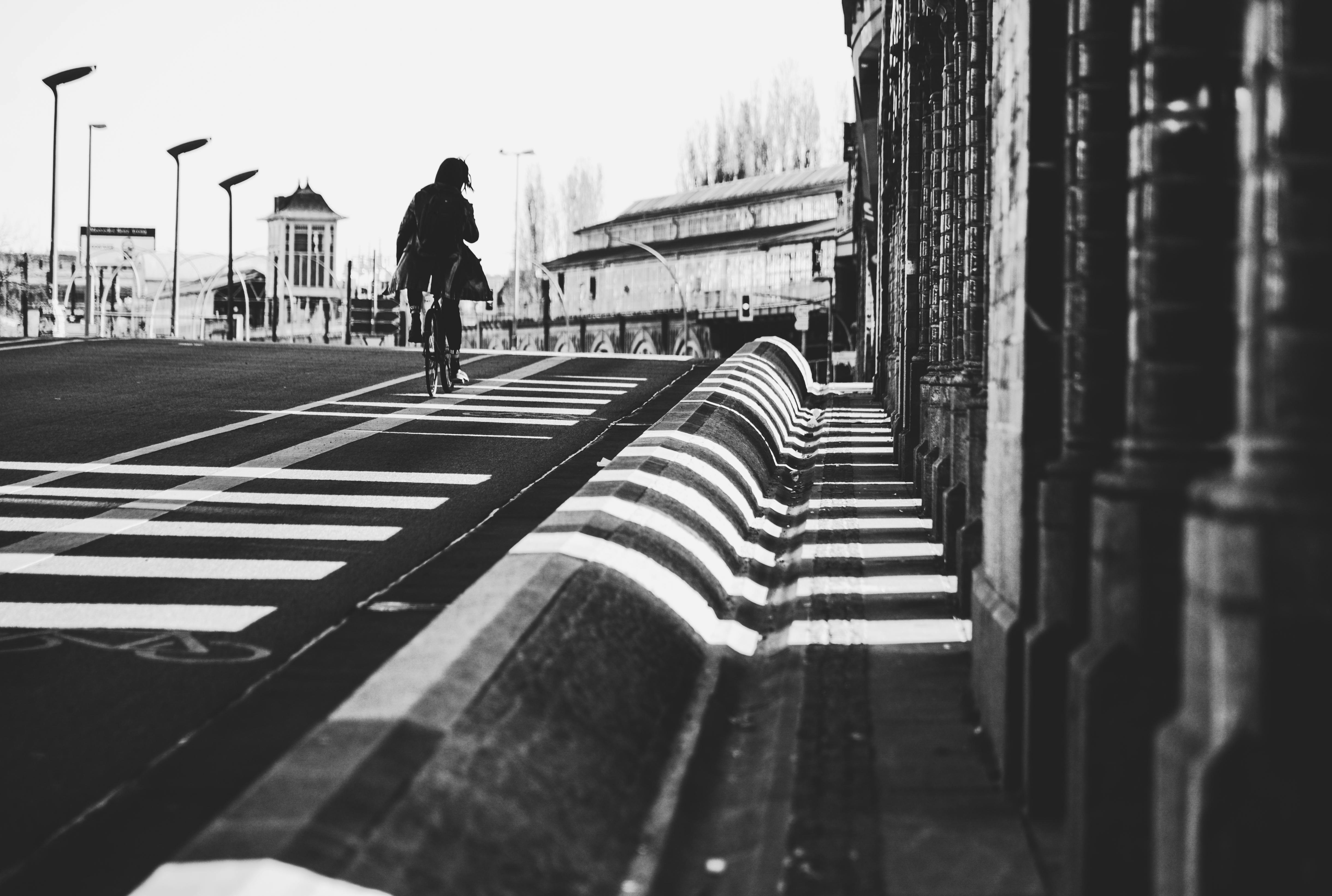 ingyenes Fekete-fehér fotó egy kerékpárosról egy városi utcán, kiemelve a városi építészetet és az árnyékokat. Stockfotó