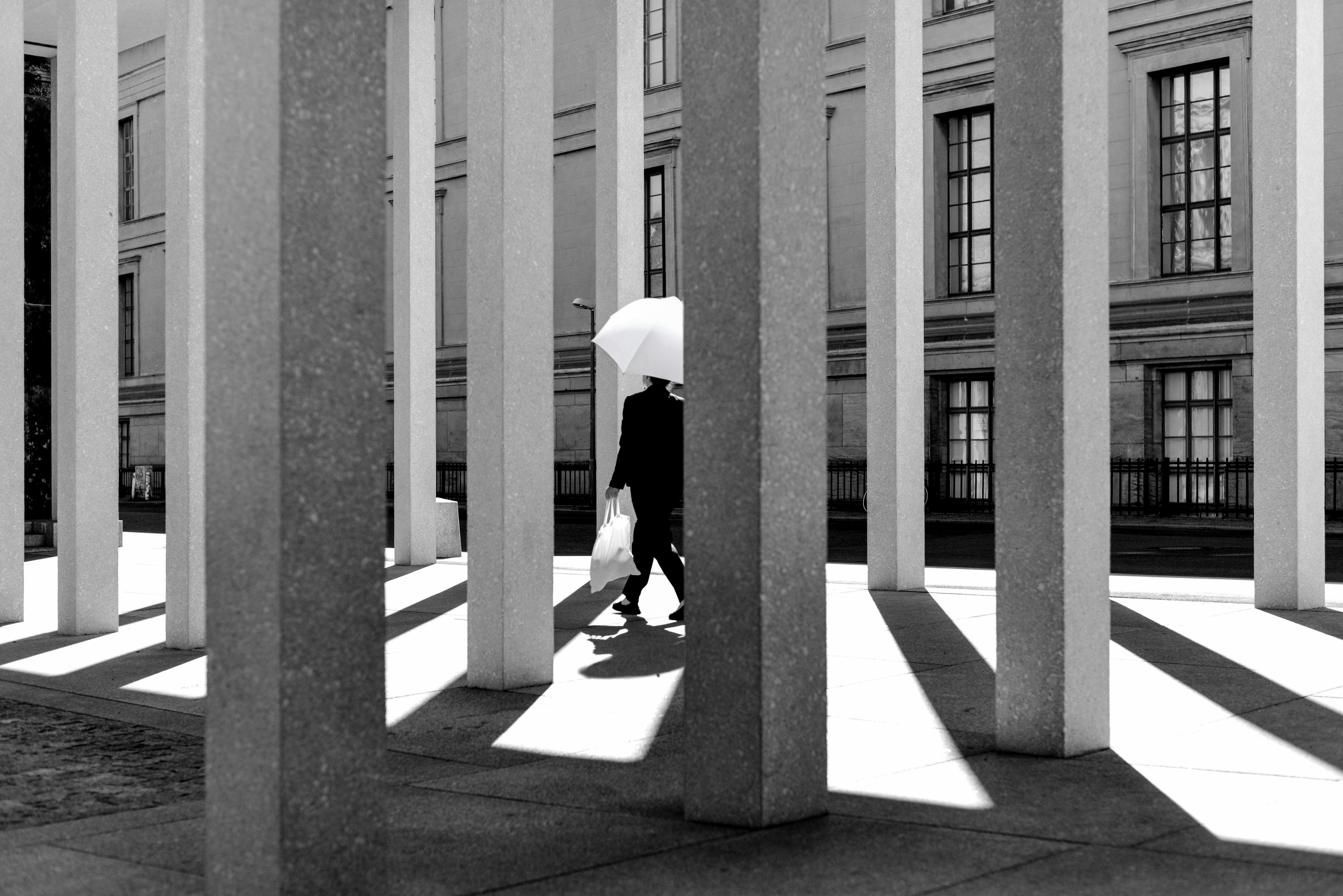 Gratis Suggestiva foto in bianco e nero di un'architettura urbana con una persona che cammina sotto un ombrello. Foto a disposizione