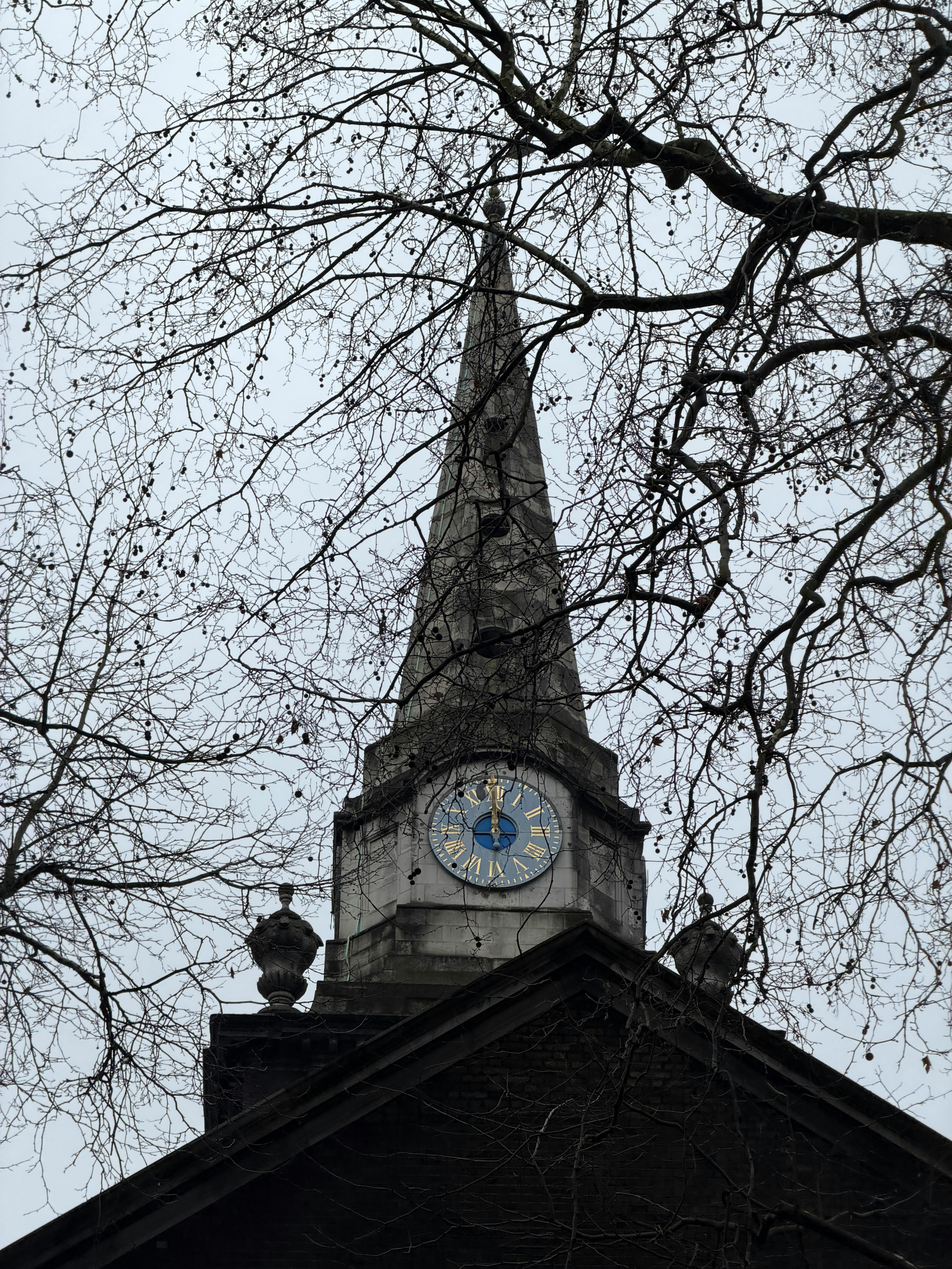 Miễn phí Cảnh tháp chuông nhà thờ St. Botolph nhìn xuyên qua những cành cây trơ trụi vào một ngày nhiều mây ở London. Ảnh lưu trữ