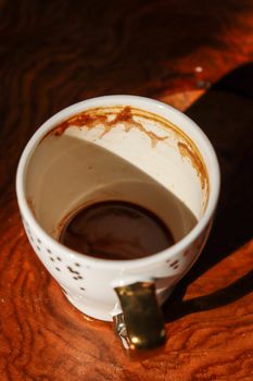 Empty coffee cup with stains and shadow in warm cafe setting, artistic lighting.