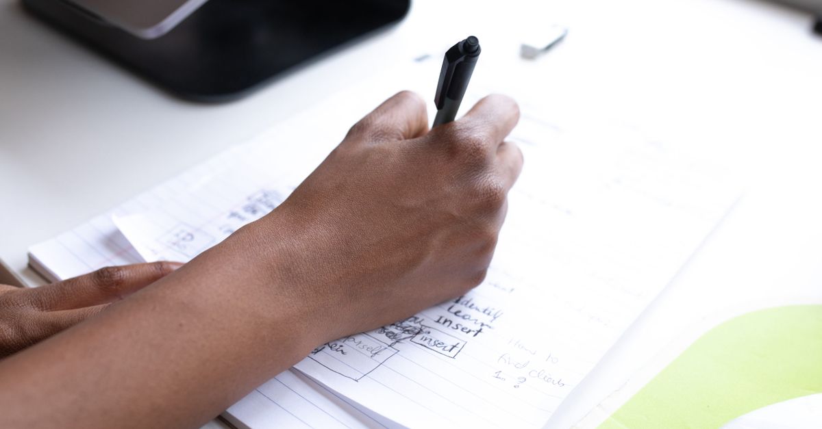 From above of crop anonymous person taking notes on papers while working at table in office