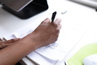 Crop faceless employee writing on paper during workday