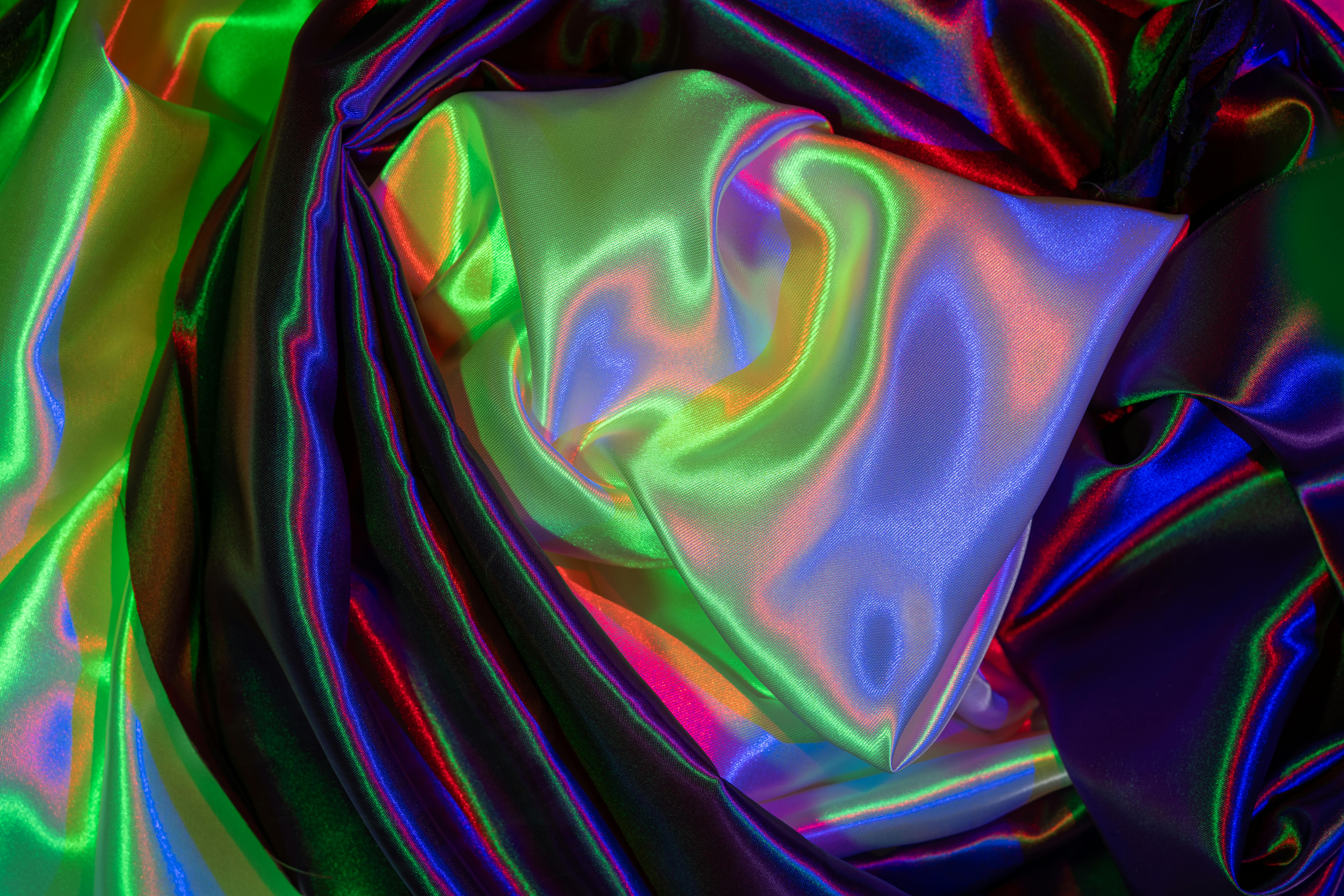 Free A close-up of vibrant satin fabric with iridescent, colorful waves creating a luxurious abstract pattern. Stock Photo