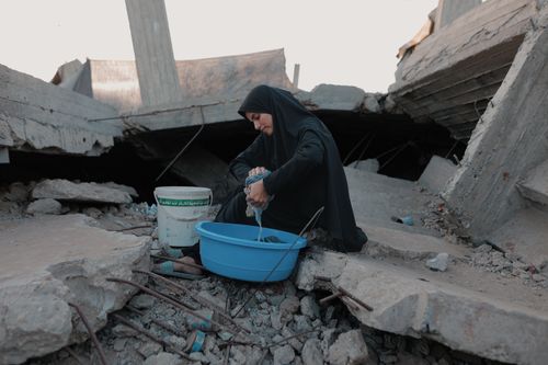 Free A woman in traditional attire washes clothes among the rubble in Gaza, depicting resilience. Stock Photo