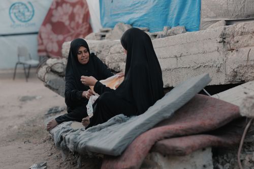 Free Two women in hijabs sit on rubble in Gaza, sharing a moment of resilience. Stock Photo