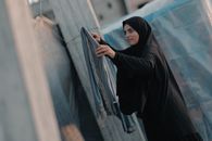 A woman in traditional clothing hangs laundry outdoors in a Gaza suburb.