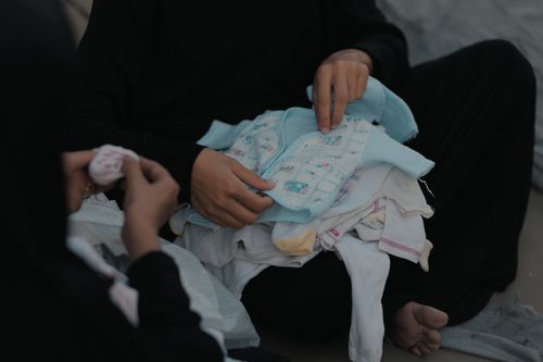 Free A woman in a Gaza refugee camp sorts a pile of baby clothes, highlighting daily life challenges. Stock Photo