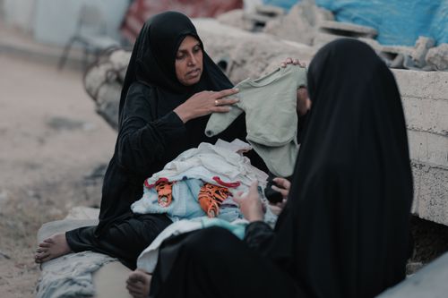 Free Two women in hijabs sorting clothes outdoors in Gaza, highlighting resilience. Stock Photo