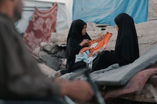 Free Two women in hijabs engage in conversation against a backdrop of rubble in Gaza. Stock Photo