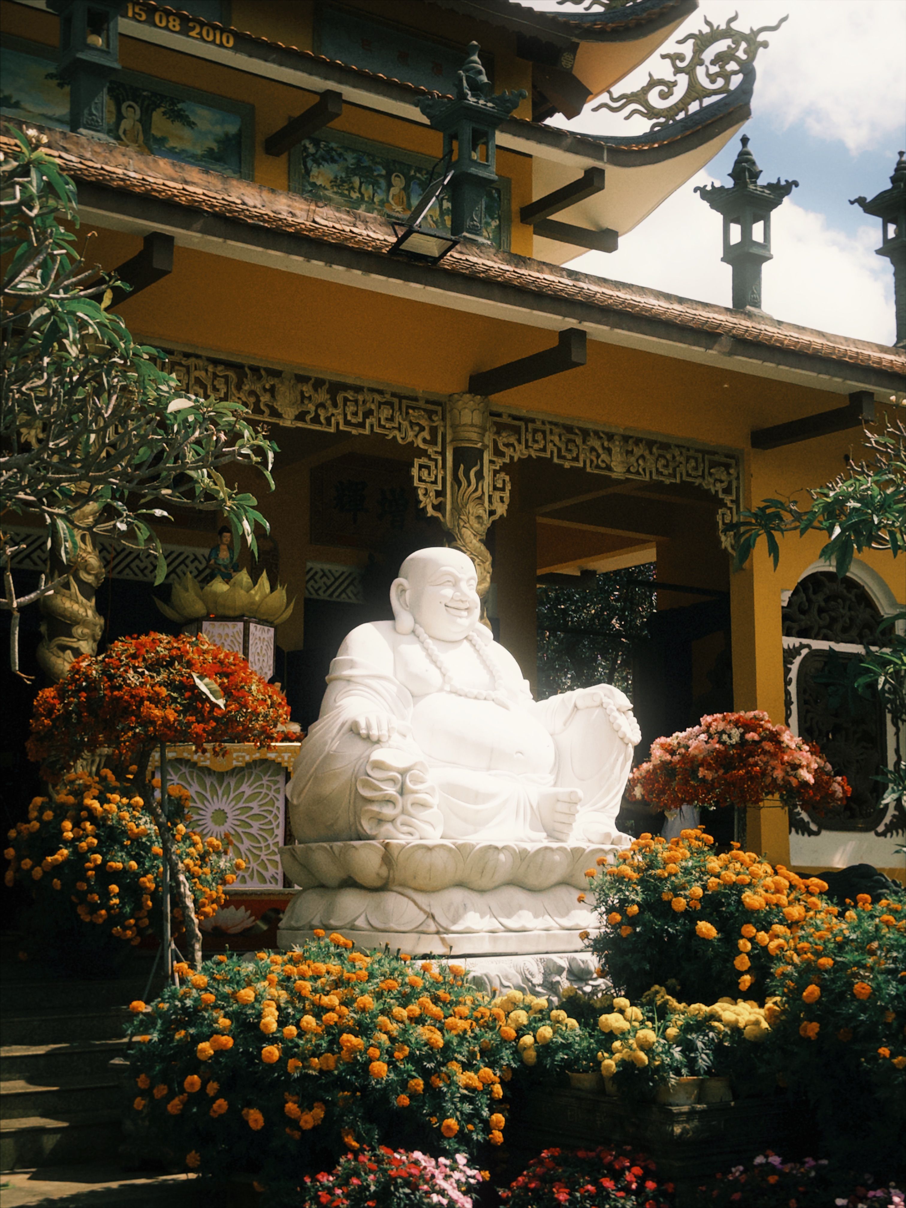 Peaceful Buddha statue surrounded by vibrant flowers at a traditional Buddhist temple.