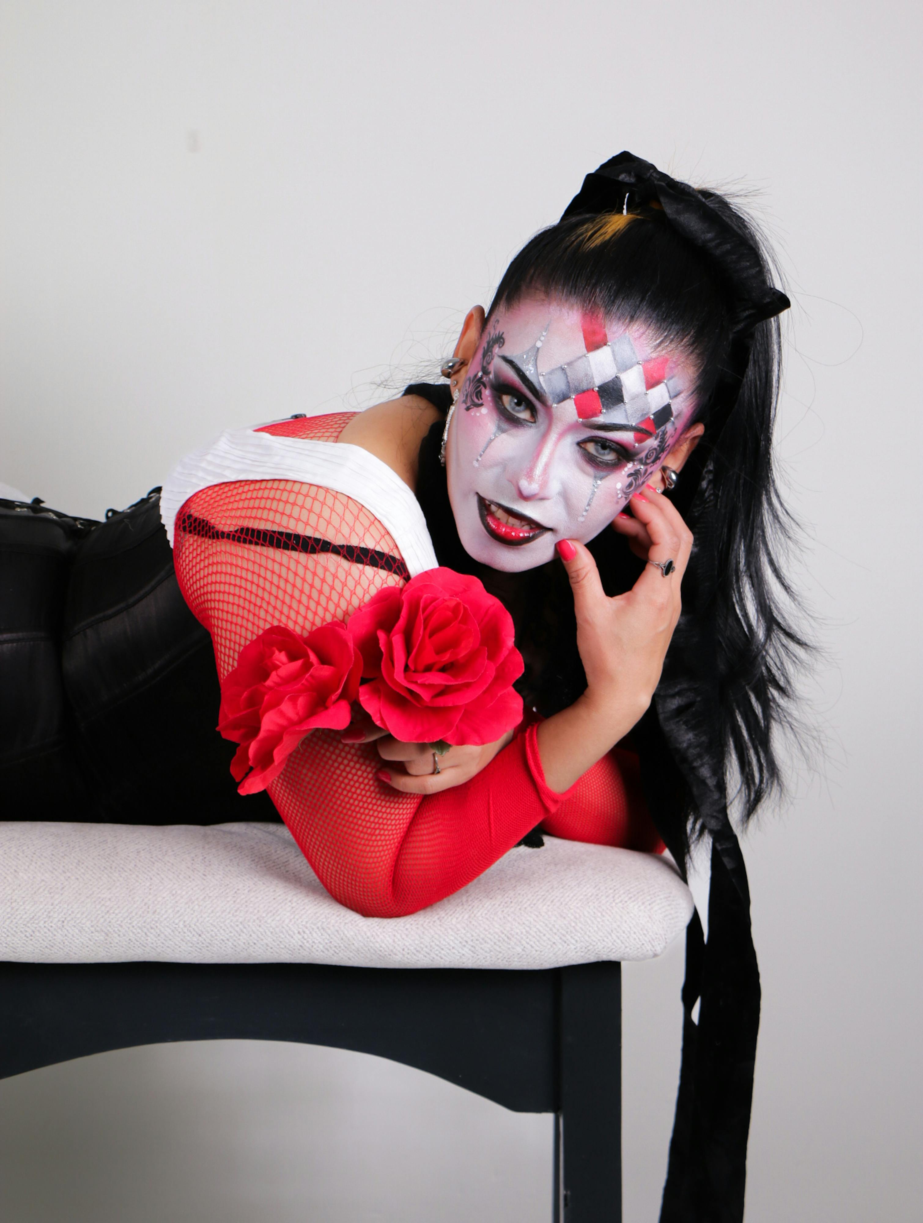 Gratis Una donna sdraiata su una panchina indossa un trucco ispirato ad Arlecchino e un costume con vivaci accenti rossi. Foto a disposizione