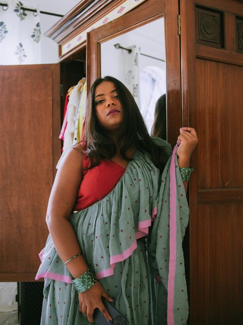 Gratis Una donna in sari verde si erge con sicurezza accanto a un armadio vintage in un interno. Cattura l'essenza della moda indiana. Foto a disposizione