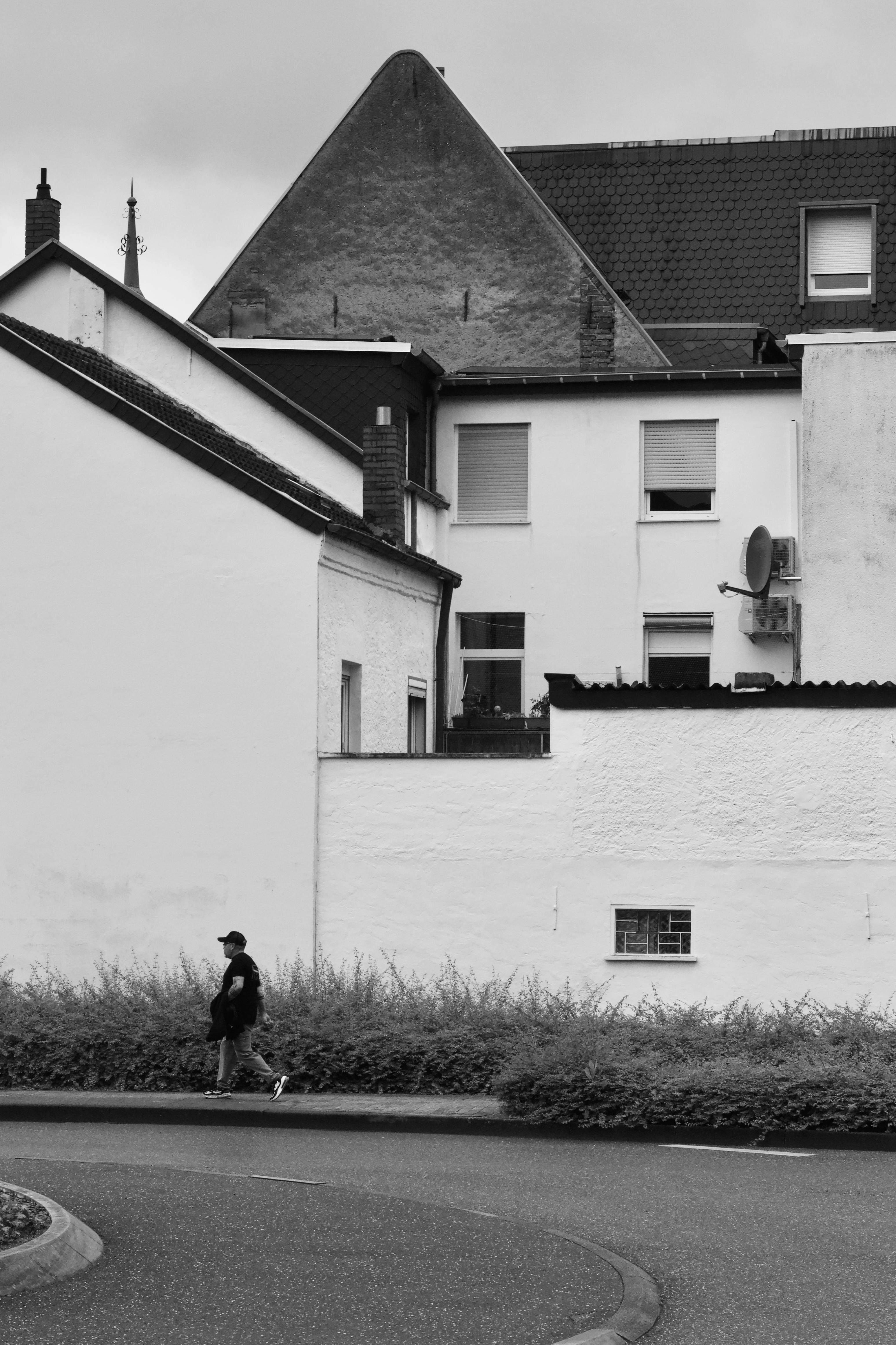 bezplatná Černobílý pohled na městskou architekturu a osamělého chodce jdoucího poblíž obytných budov. Základová fotografie