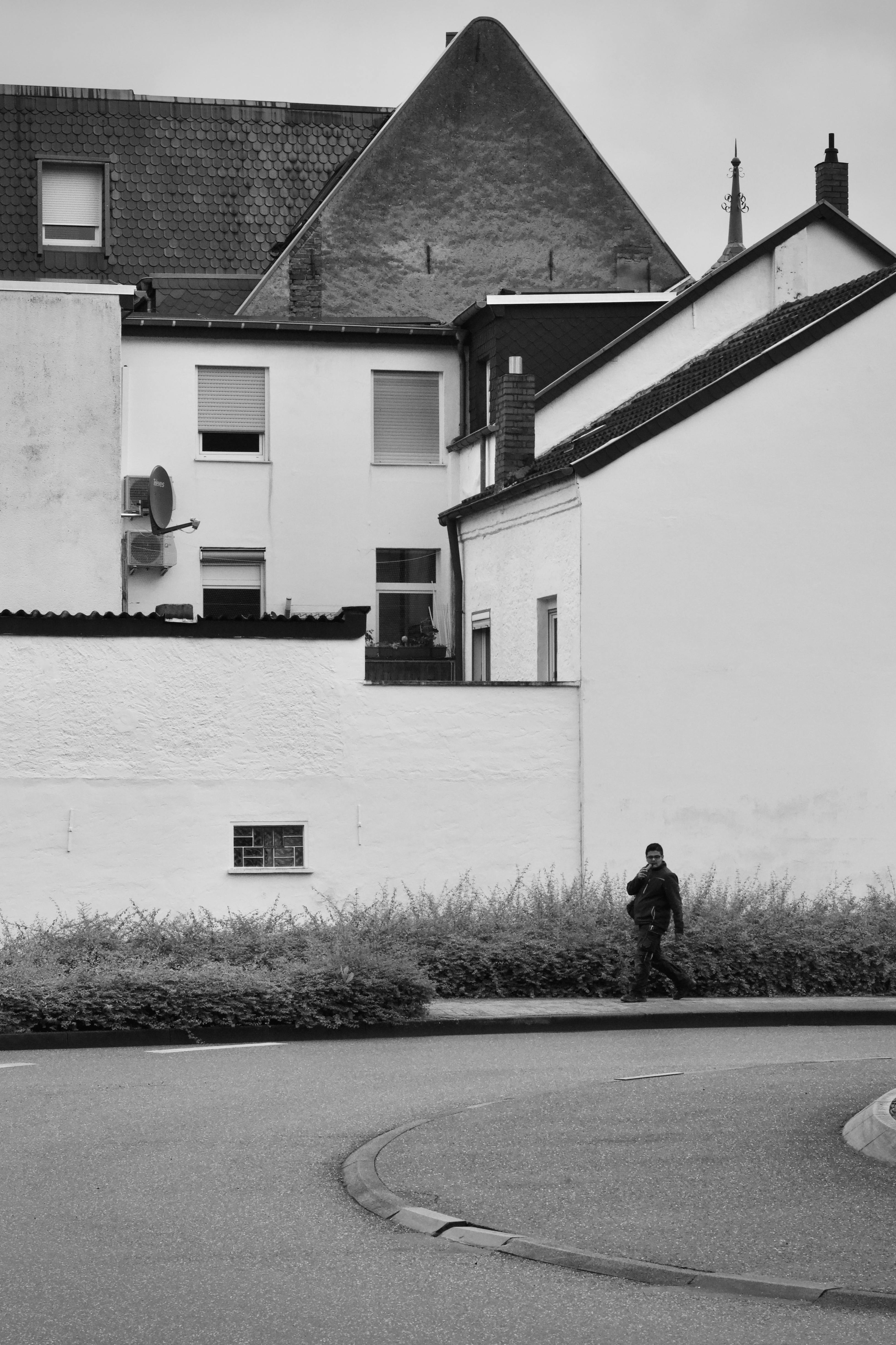 bezplatná Osamělý dospělý člověk kráčí po městské ulici vedle bílých budov. Monochromatický tón. Základová fotografie