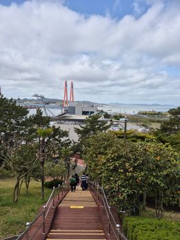A scenic view of a pathway leading down to a waterfront with a cable-stayed bridge in the distance.